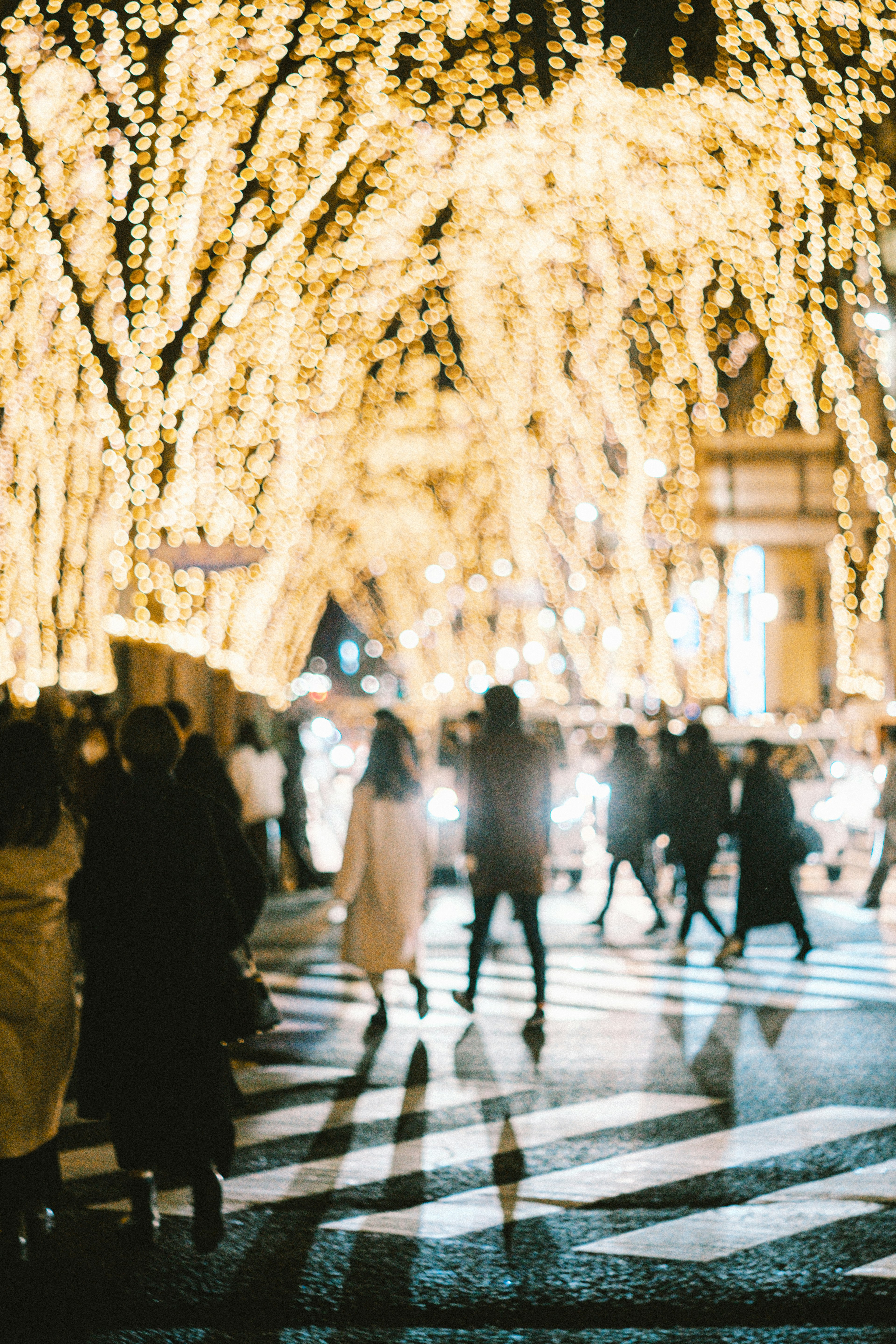 People crossing a street under bright holiday lights at night