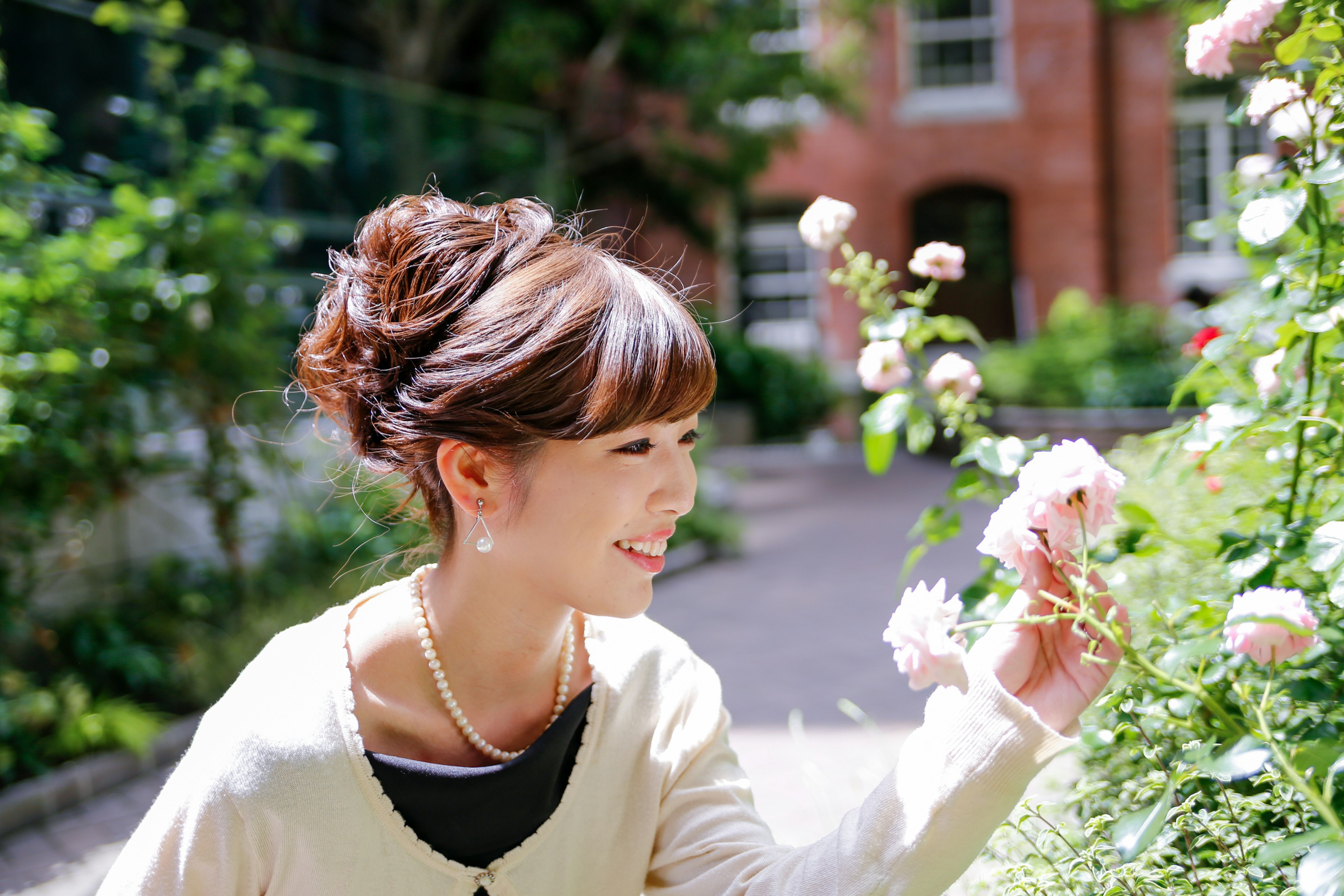 A woman smiling while touching flowers in a lush green garden with bright sunlight