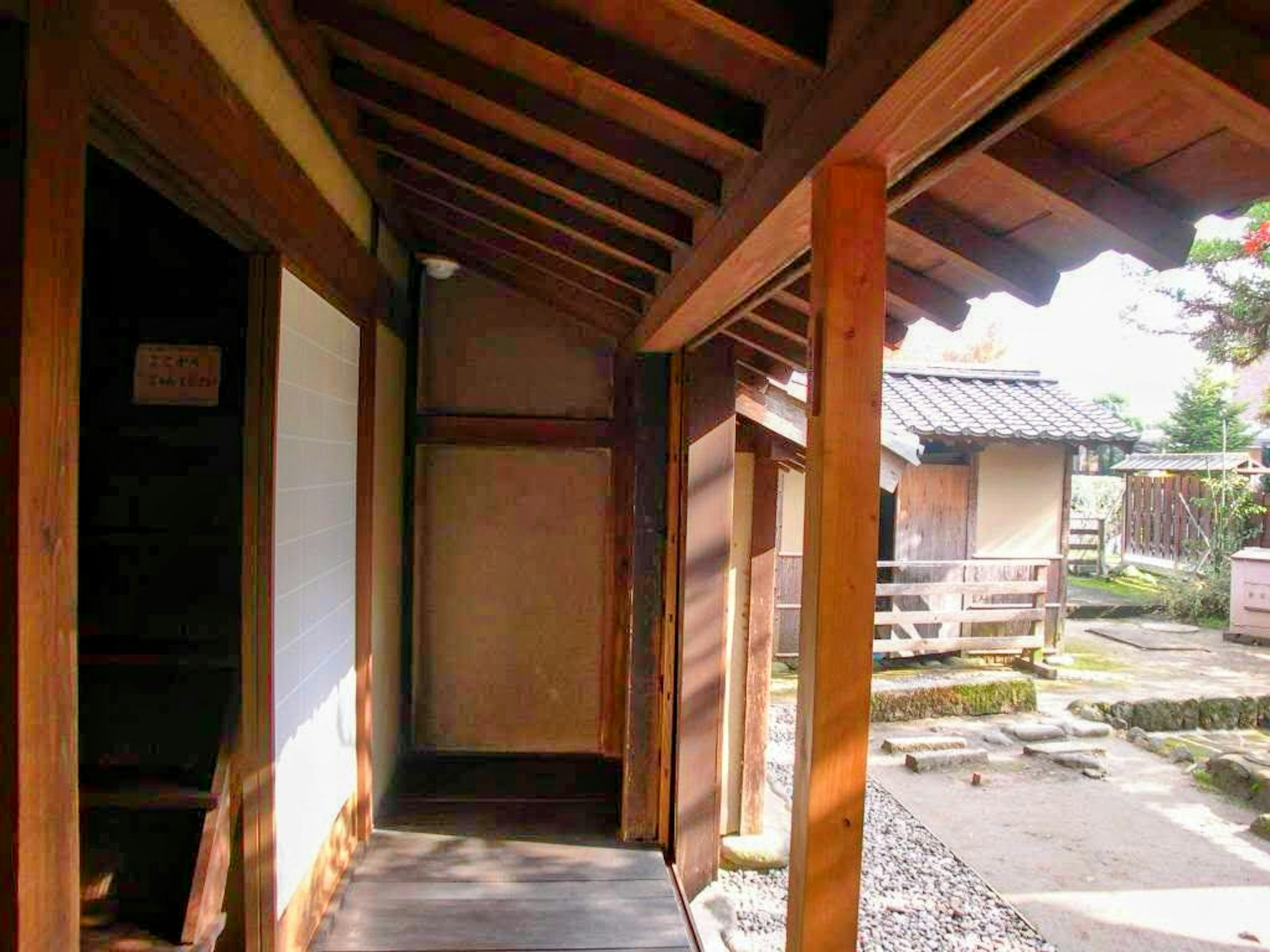 Koridor Jepang tradisional dengan balok dan tiang kayu serta pemandangan rumah terdekat