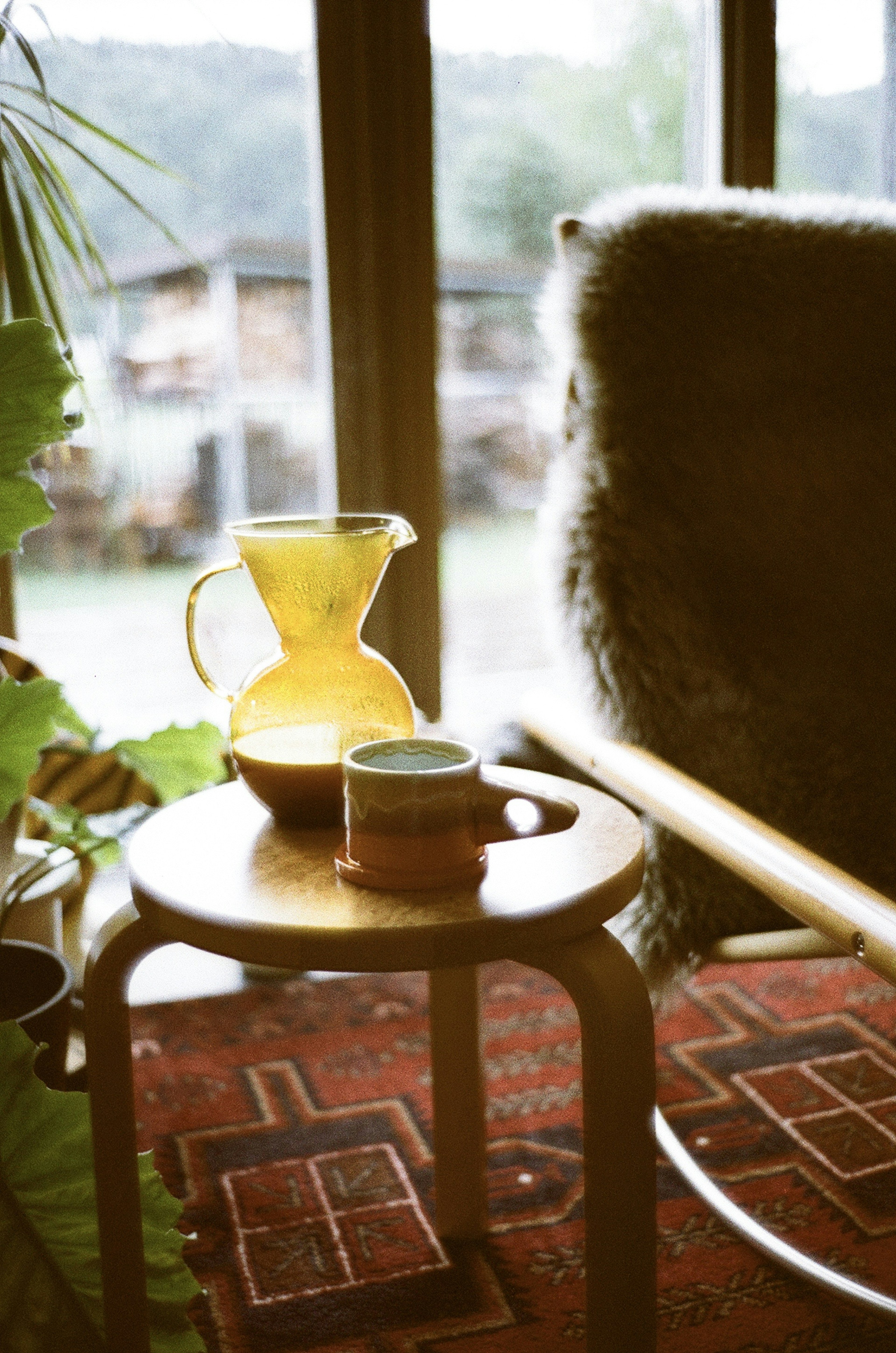 Ein Holztisch mit einer gelben Karaffe und einer Keramiktasse am Fenster