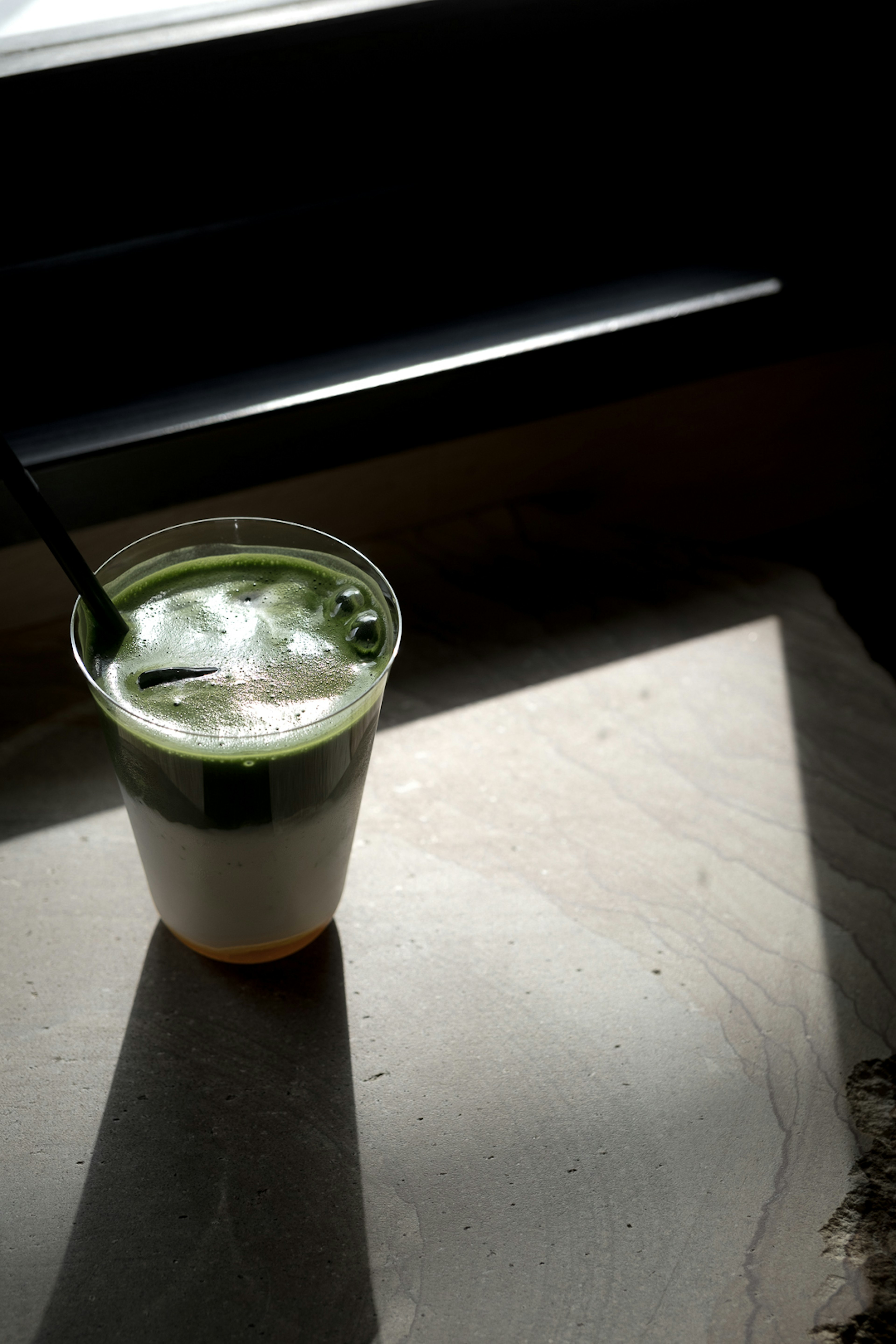 Una bebida con capas de té verde y crema colocada junto a una ventana