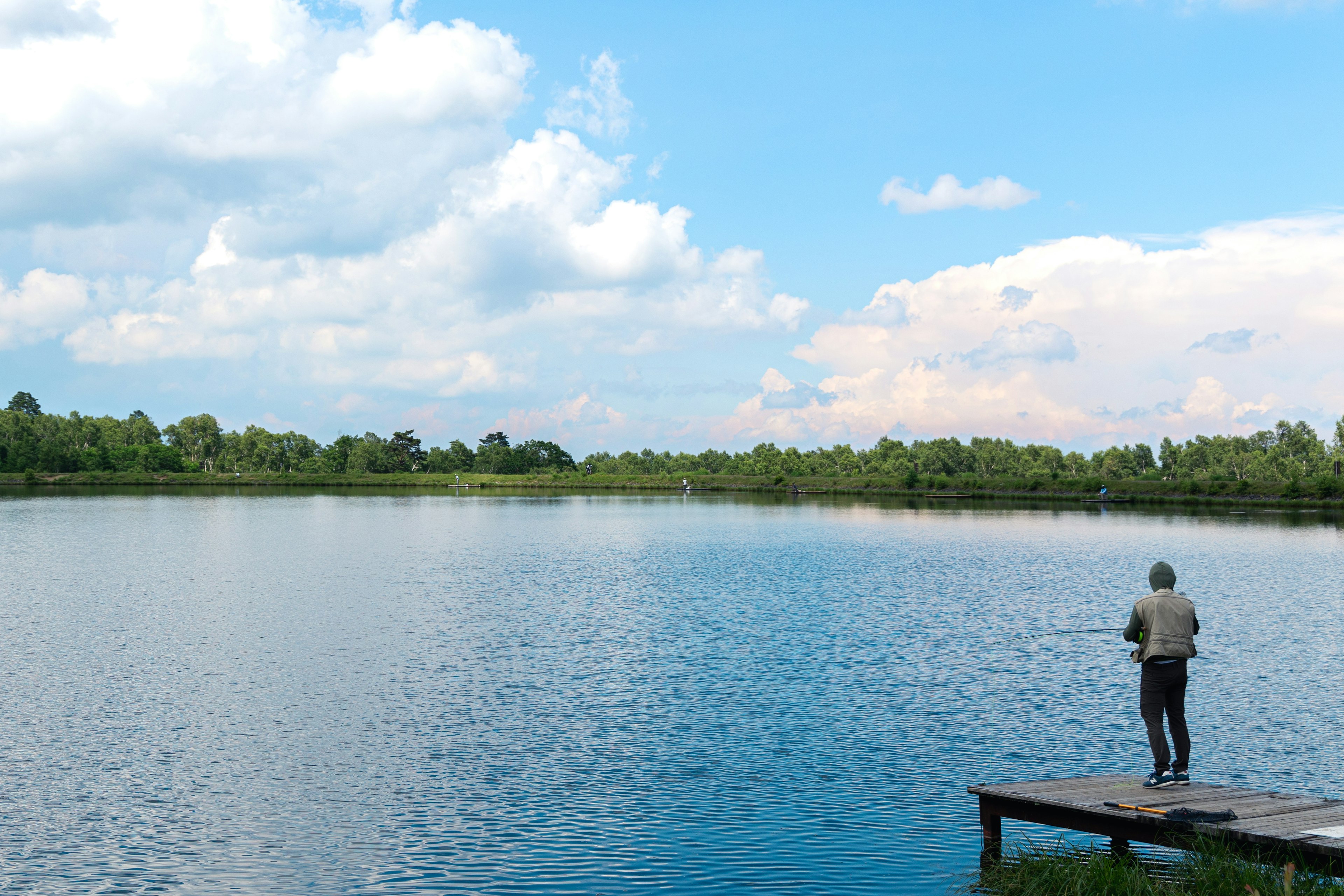 Pescador de pie al borde de un lago bajo un cielo azul