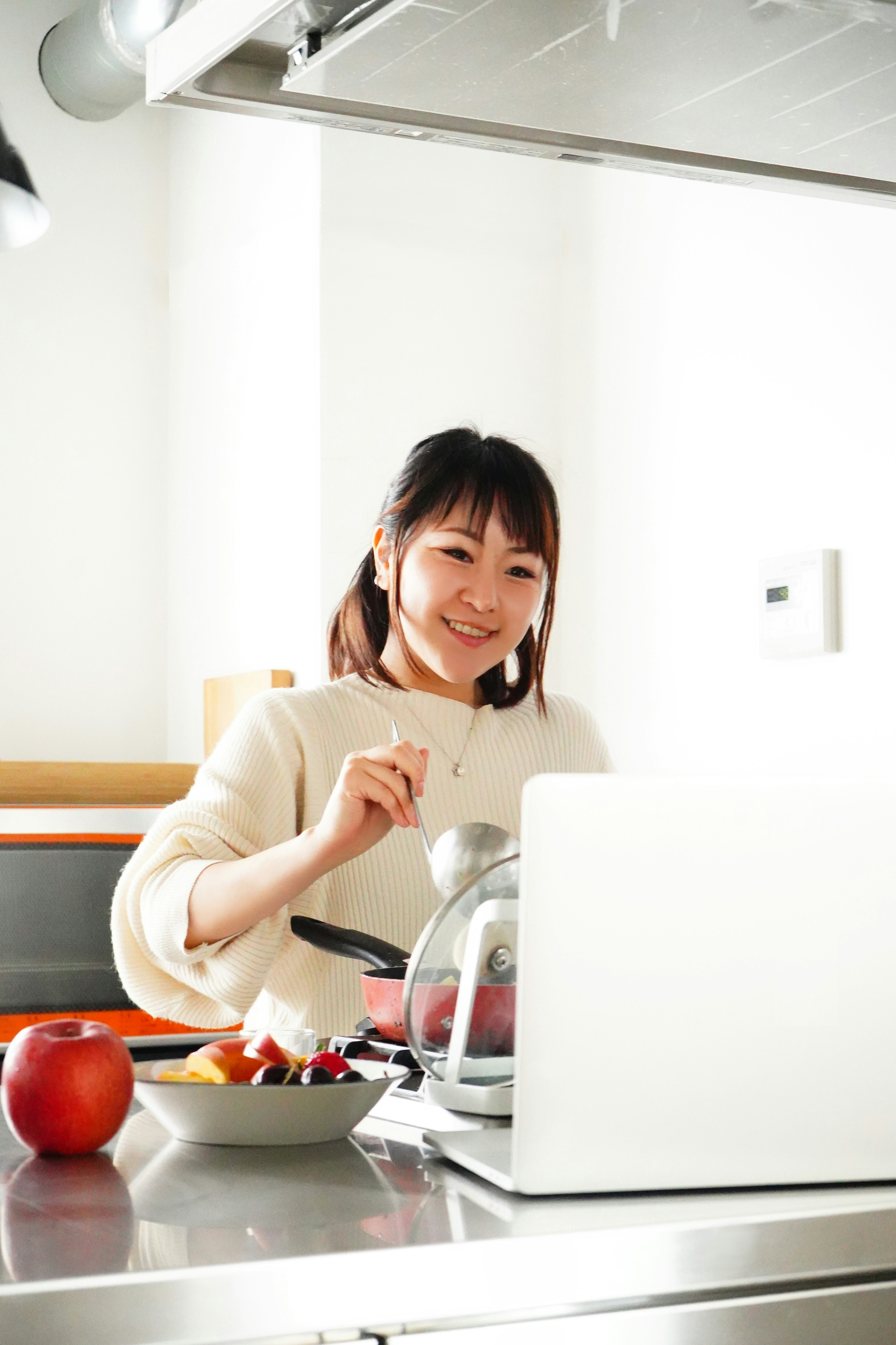 Mujer sonriente preparando comida en una cocina con una computadora portátil