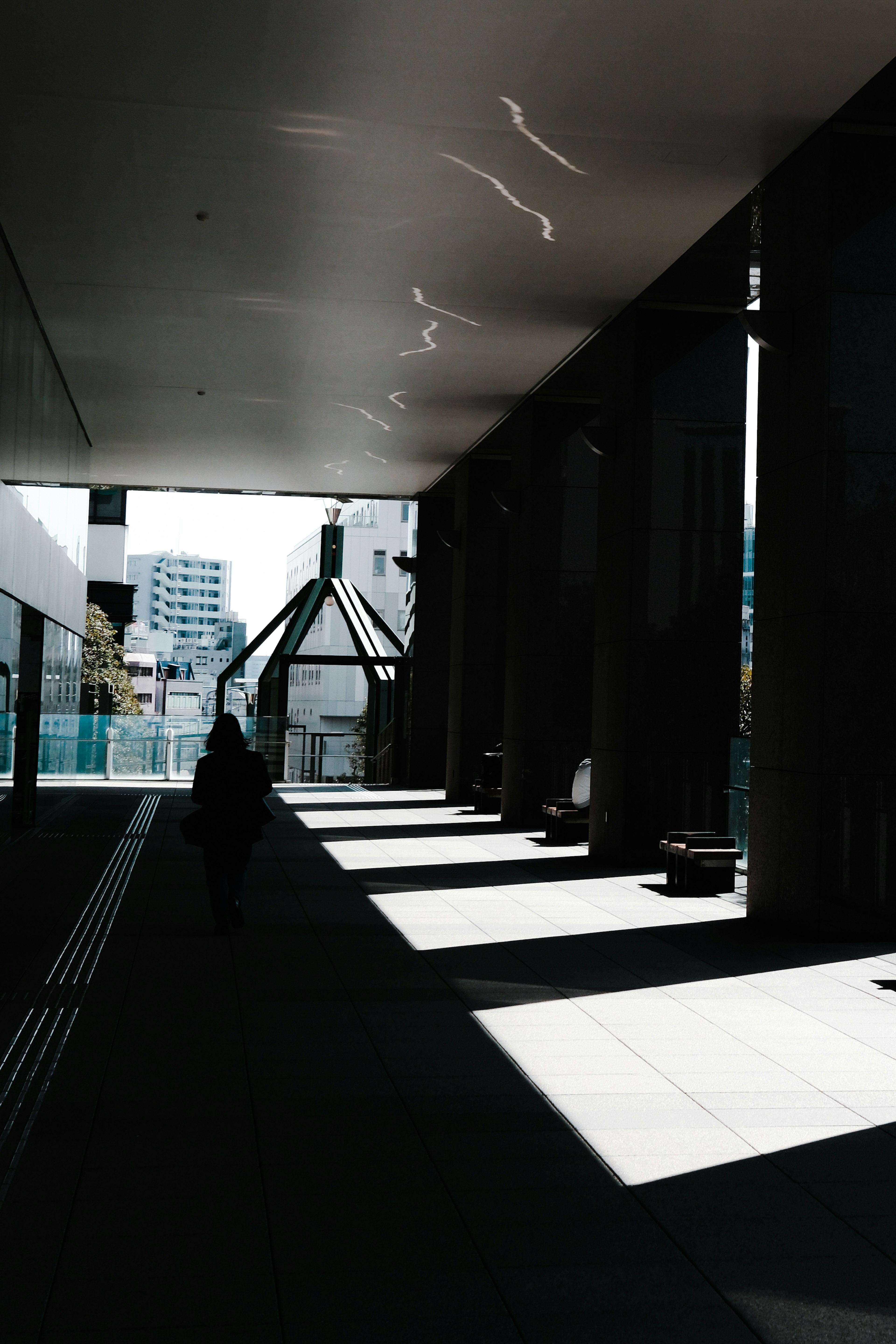 Silhouette seorang di koridor gelap dengan kontras mencolok antara cahaya dan bayangan dalam arsitektur modern