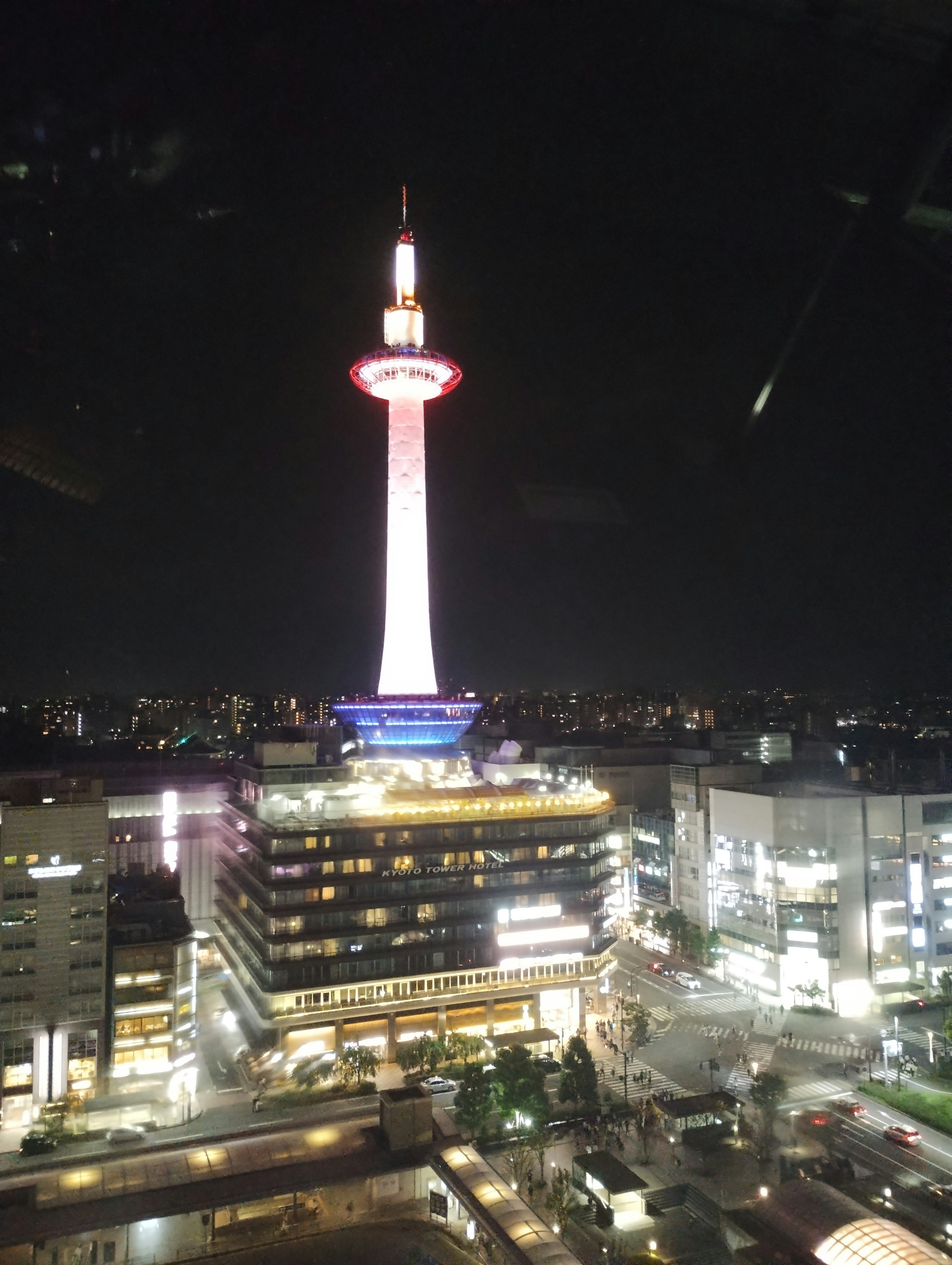 Kyoto Tower illuminated at night with surrounding buildings