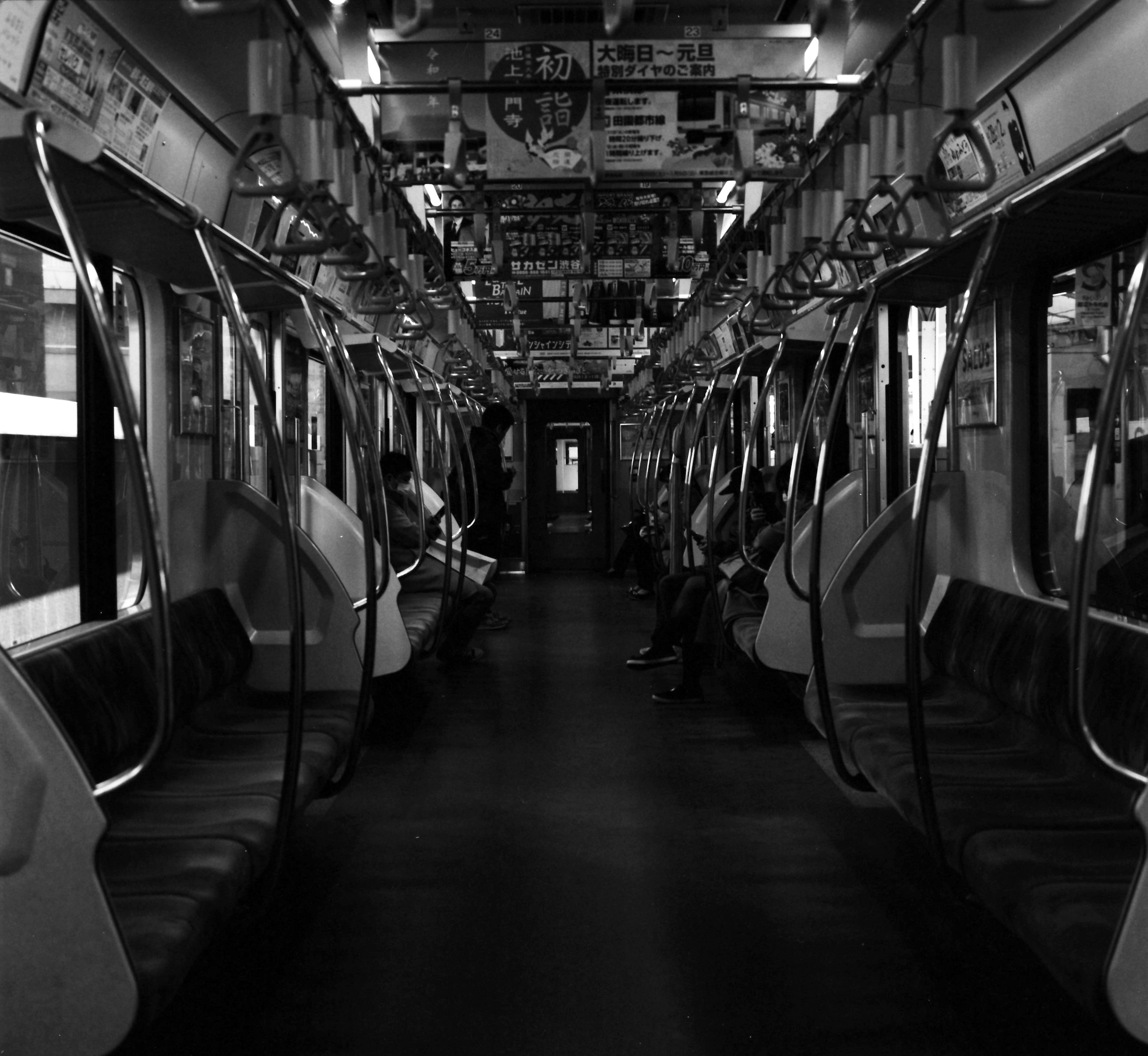 Interior of a black and white subway train with noticeable empty seats and a quiet atmosphere