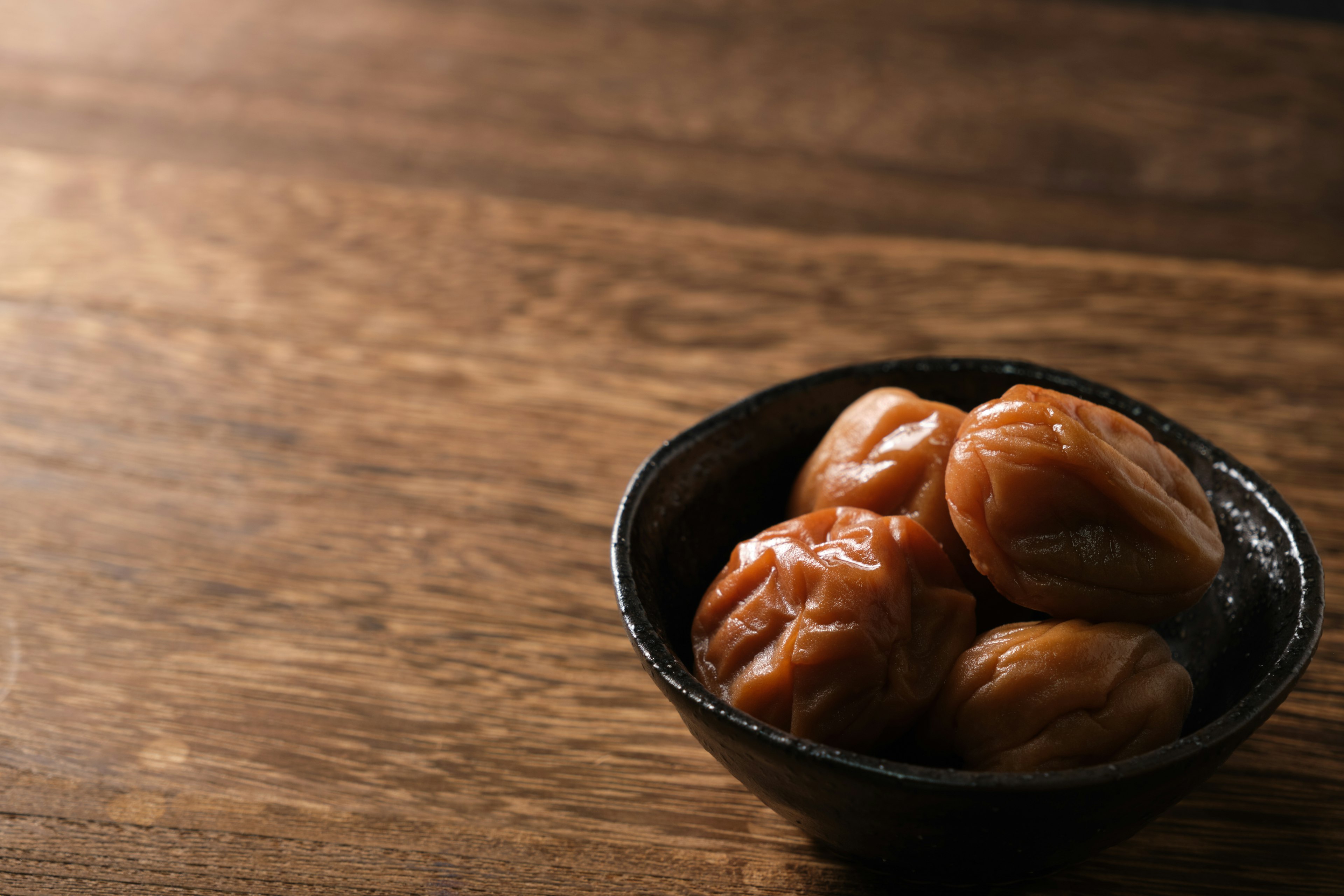 Plum kering dalam mangkuk hitam di atas meja kayu