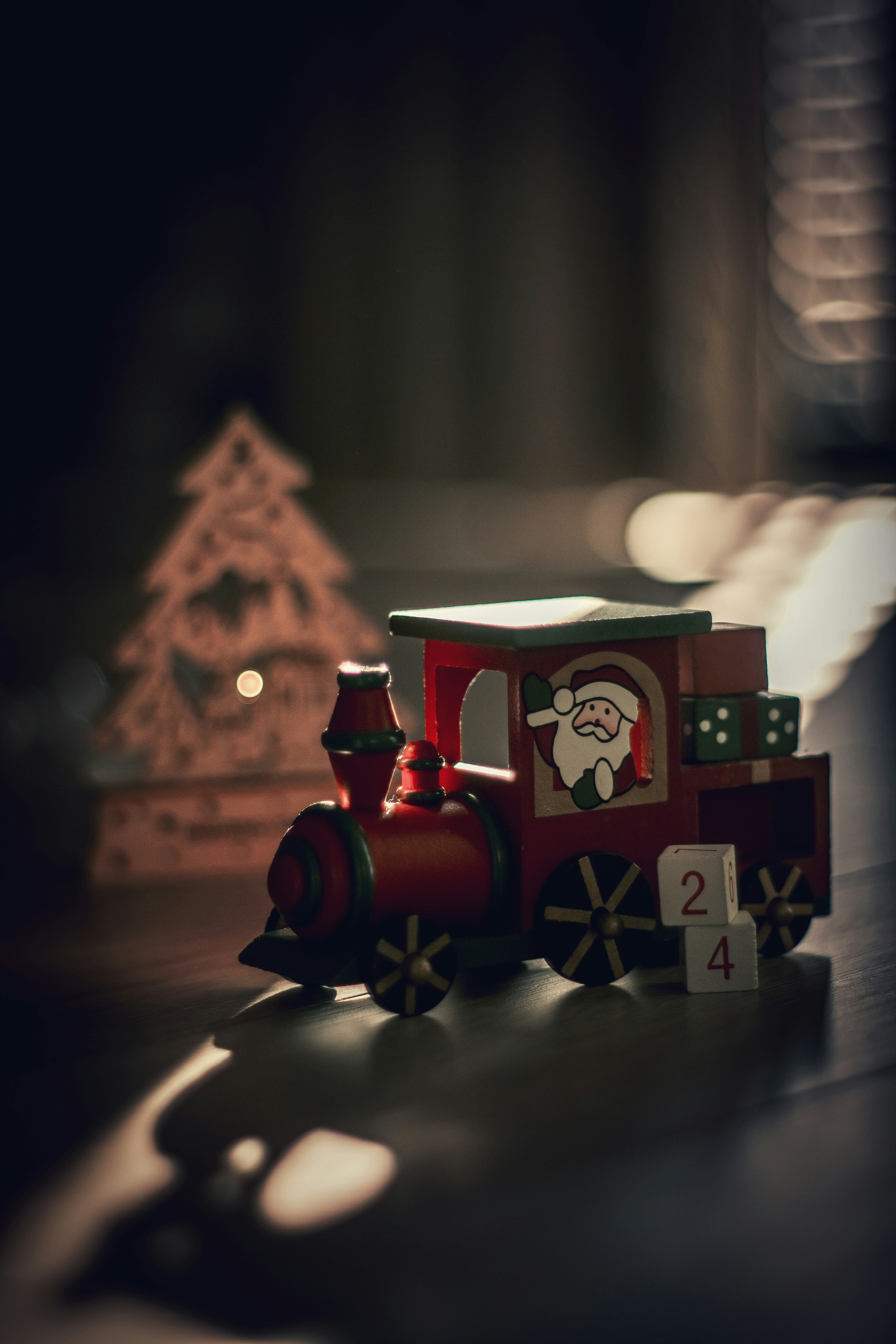 A red toy train featuring Santa and a wooden Christmas tree in a dimly lit setting