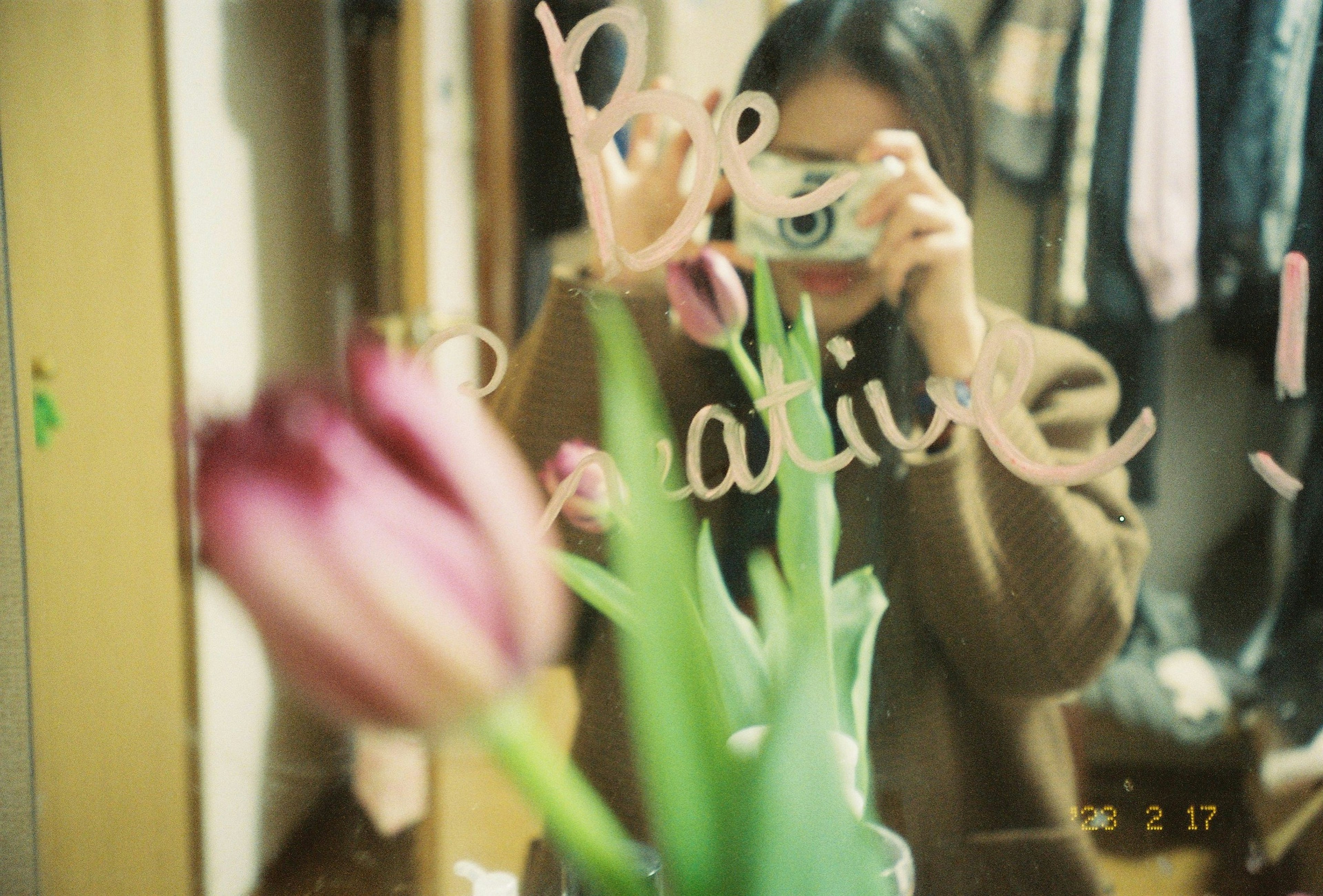 Une femme tenant un appareil photo devant un miroir avec une fleur de tulipe