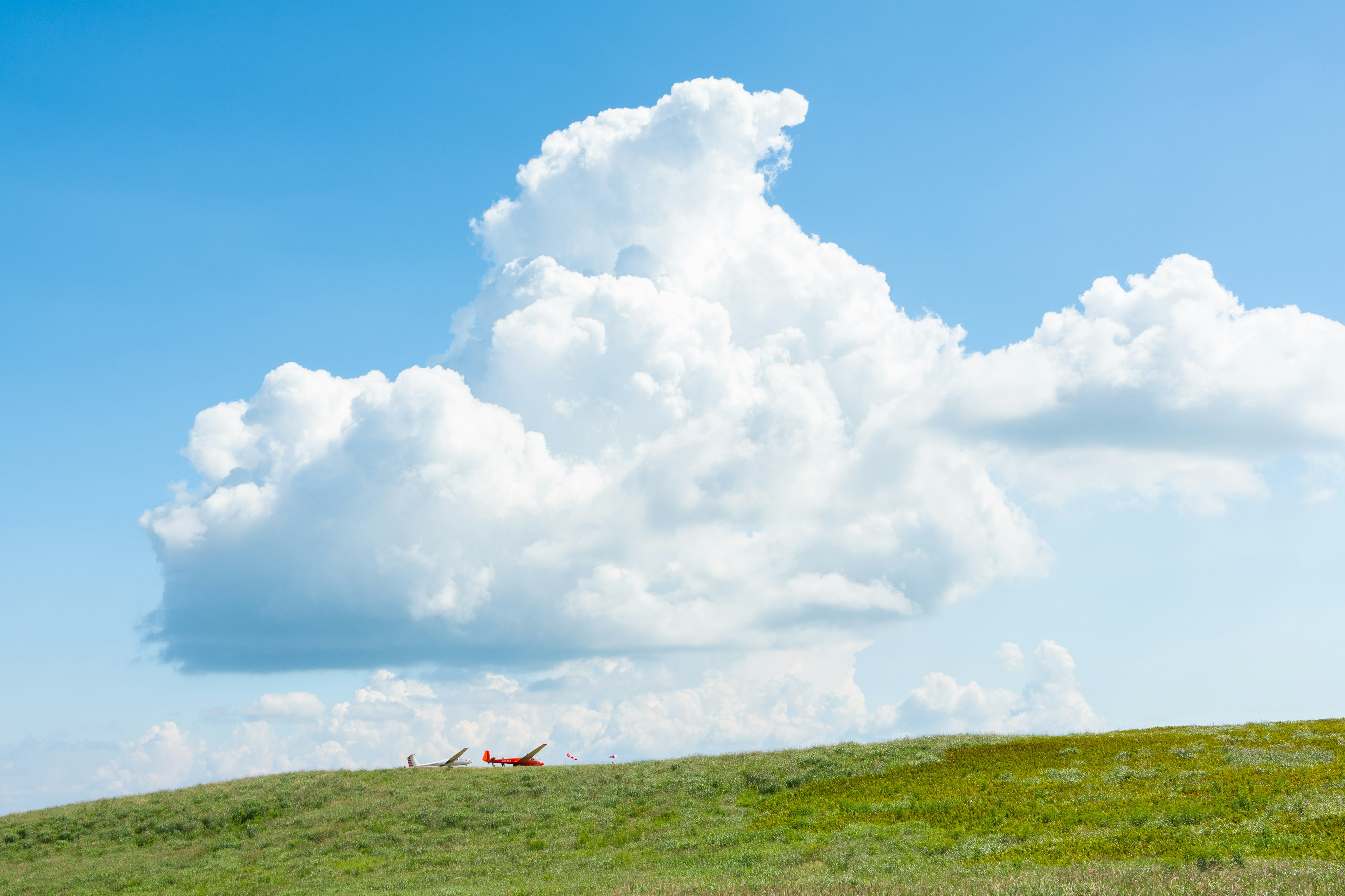 Un paisaje con cielo azul y una gran nube sobre una colina verde