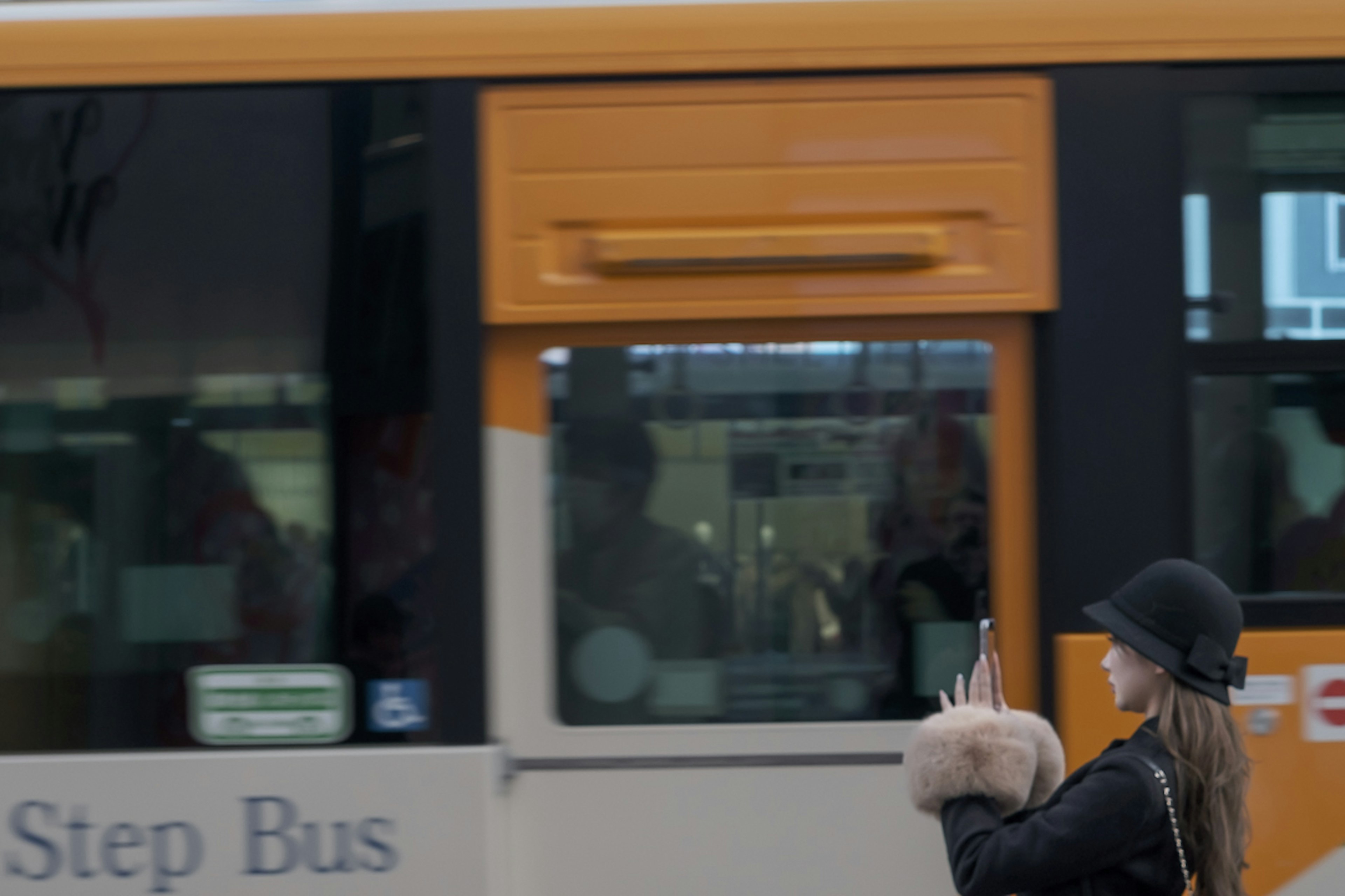 Seorang wanita melambaikan tangan kepada bus oranye dengan topi stylish