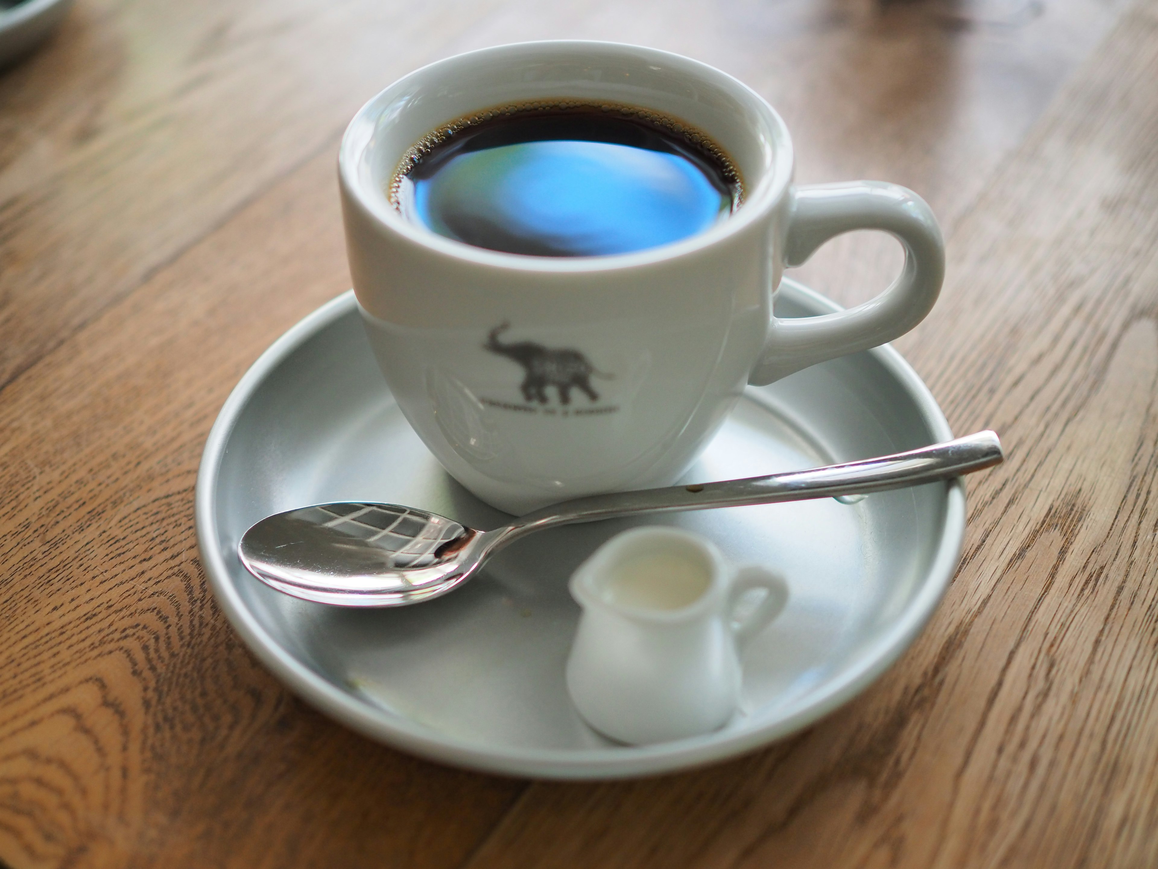 Coffee in a white cup with an elephant logo and a small cream pitcher on a saucer