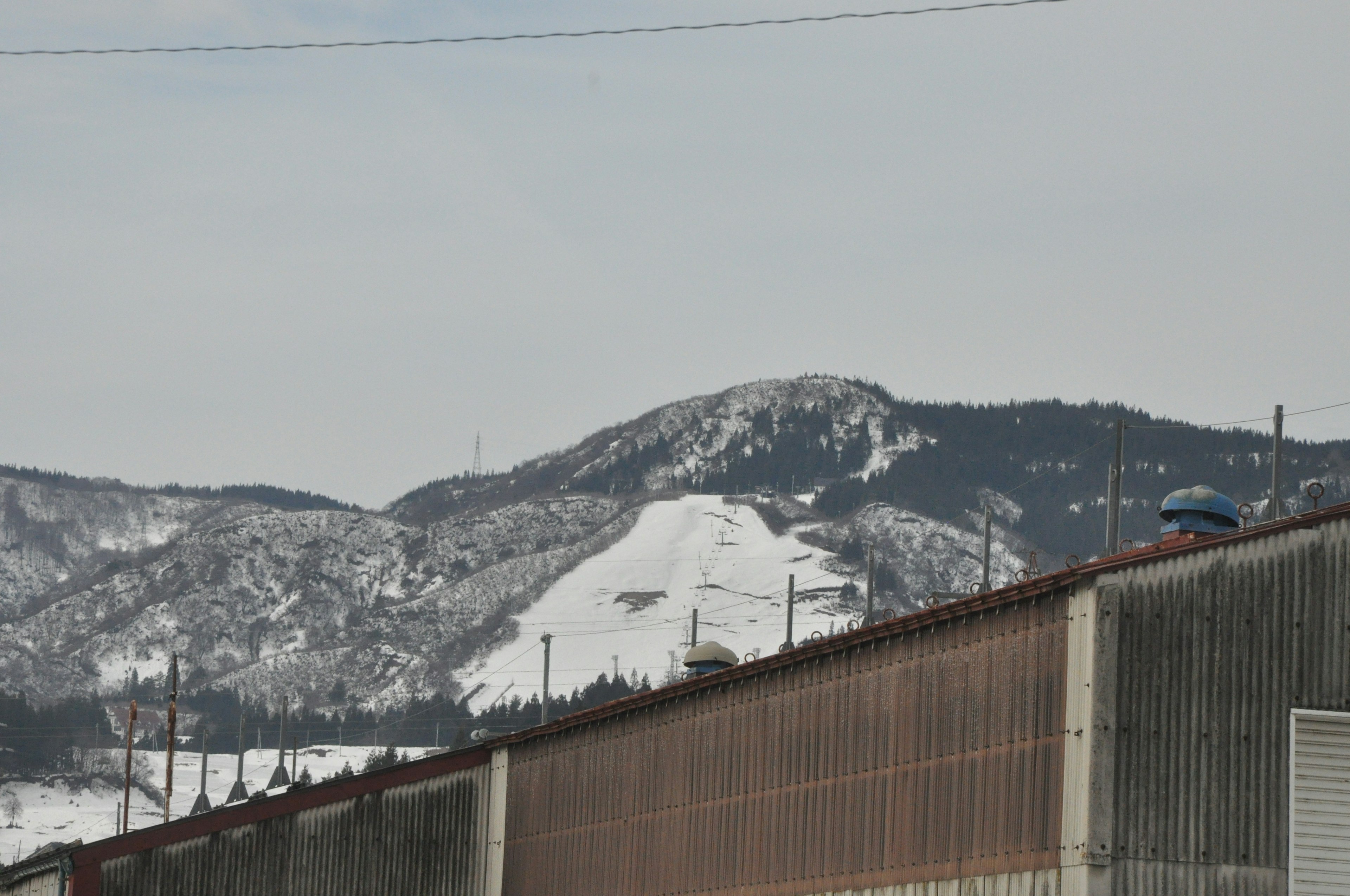 Snow-covered mountain with a factory wall in the foreground