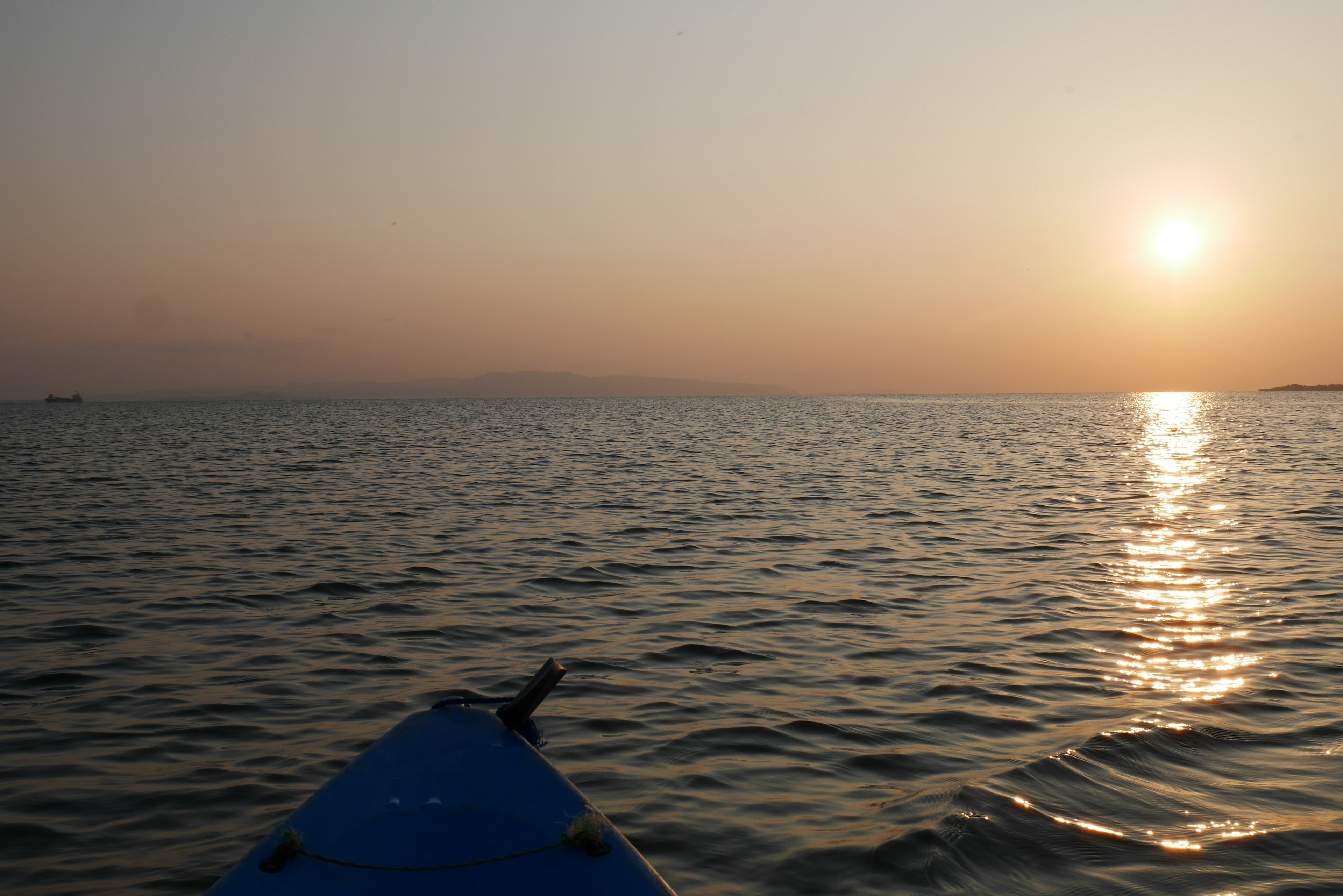 A blue kayak floating on water with sunset reflections over the sea