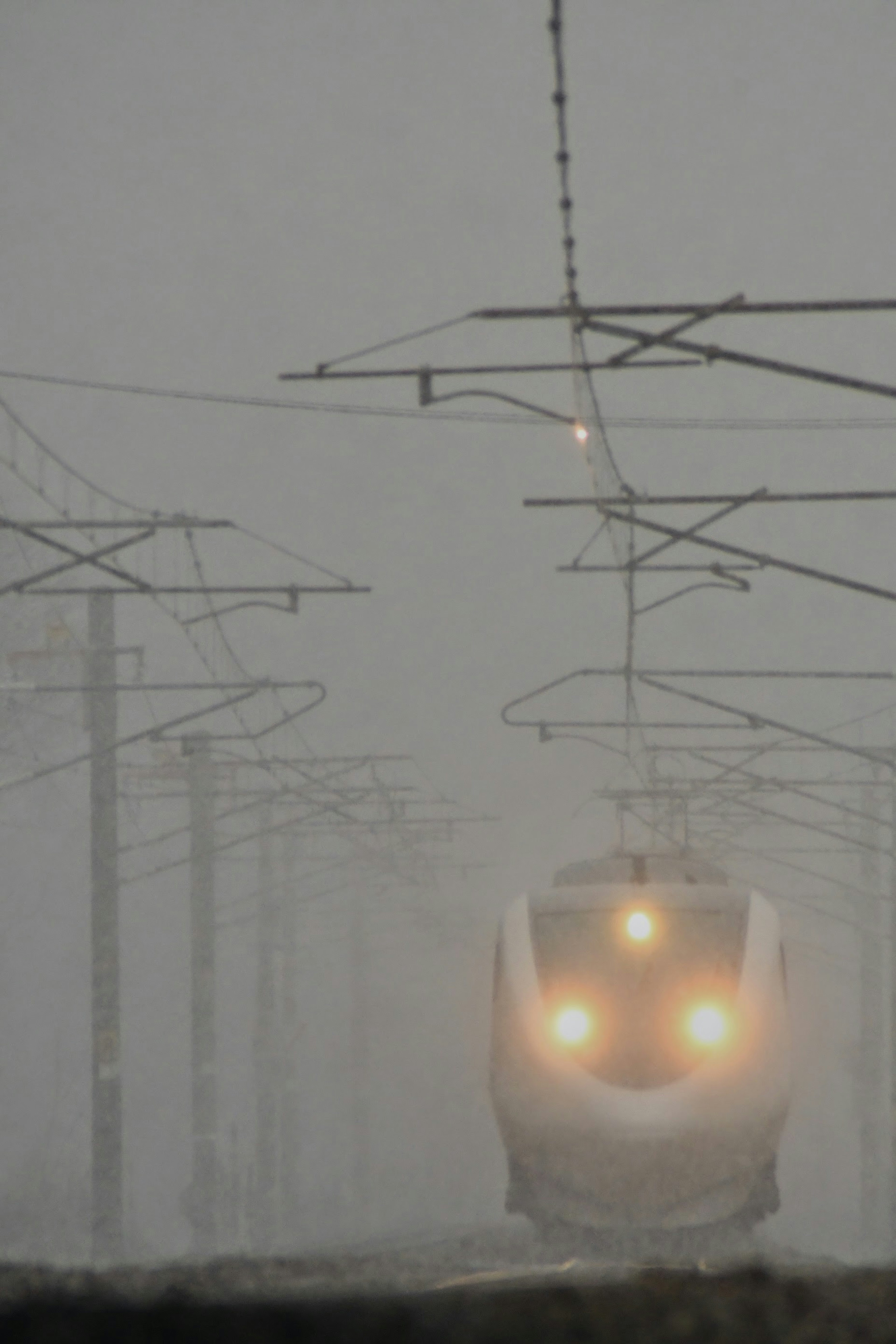 Shinkansen train approaching in fog with visible tracks and overhead lines