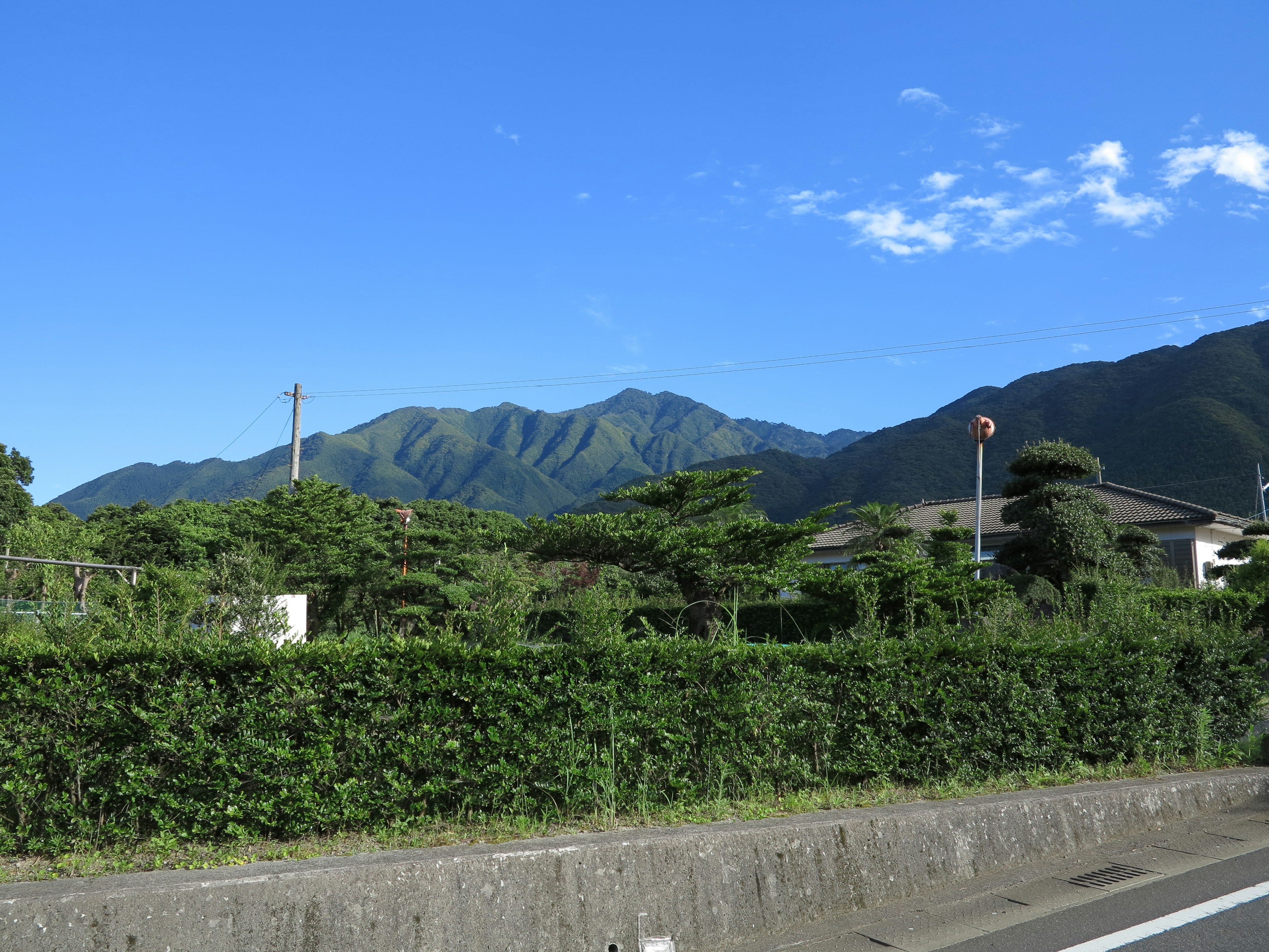 Landscape featuring green mountains under a clear blue sky with rural houses and lush greenery