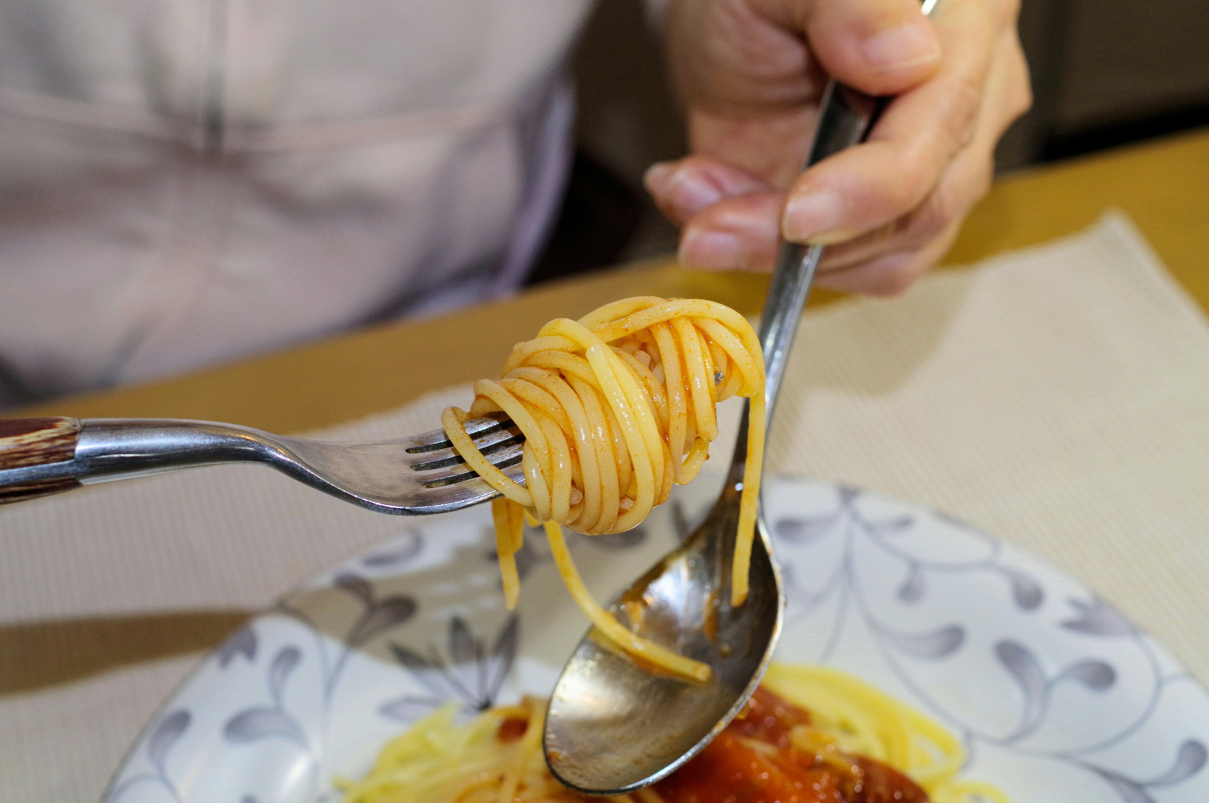 Một bàn tay cuộn mì spaghetti bằng nĩa và thìa