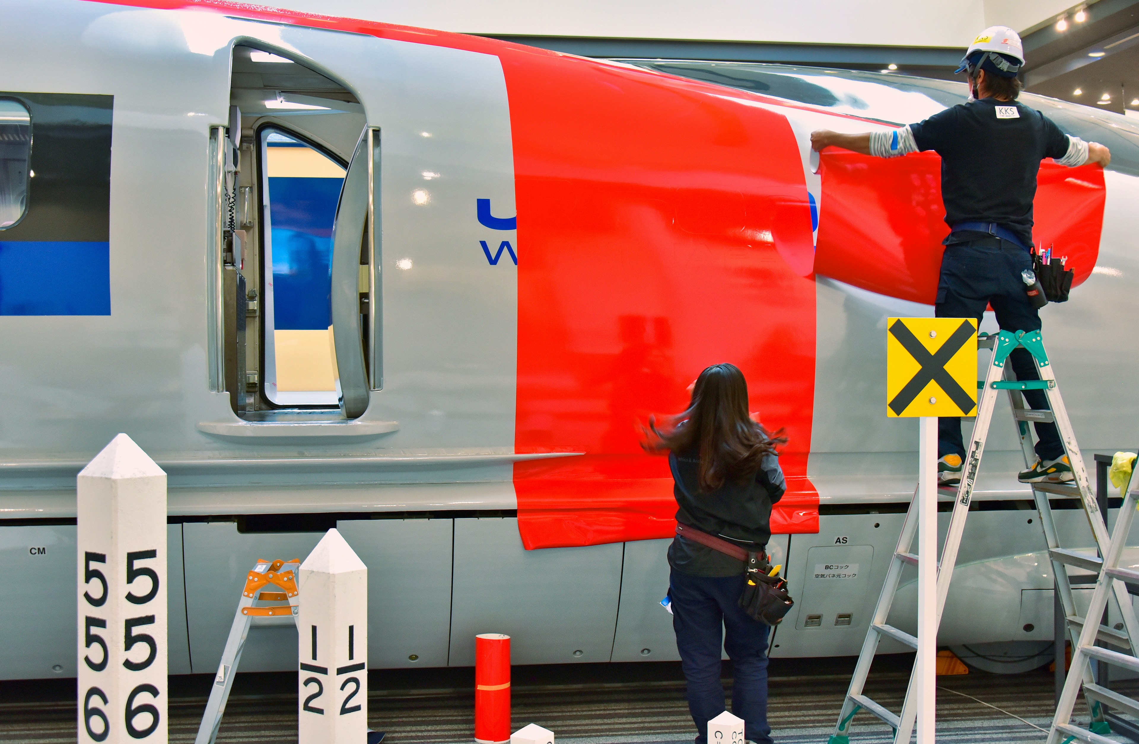 Lavoratori che applicano una pellicola rossa sul lato di un treno ad alta velocità