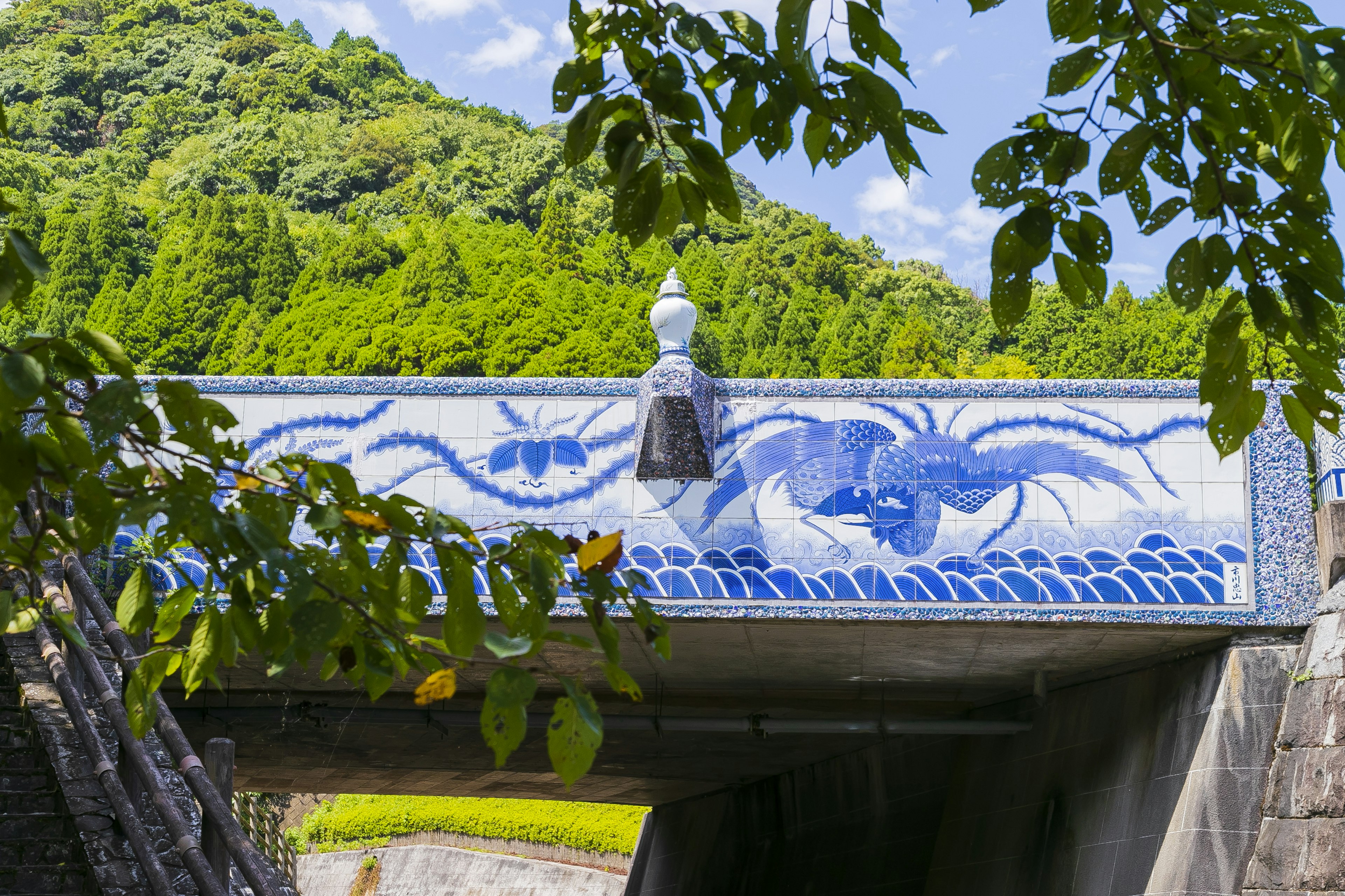 Pont avec un design de vagues bleues et un pilier décoratif blanc entouré de montagnes vertes