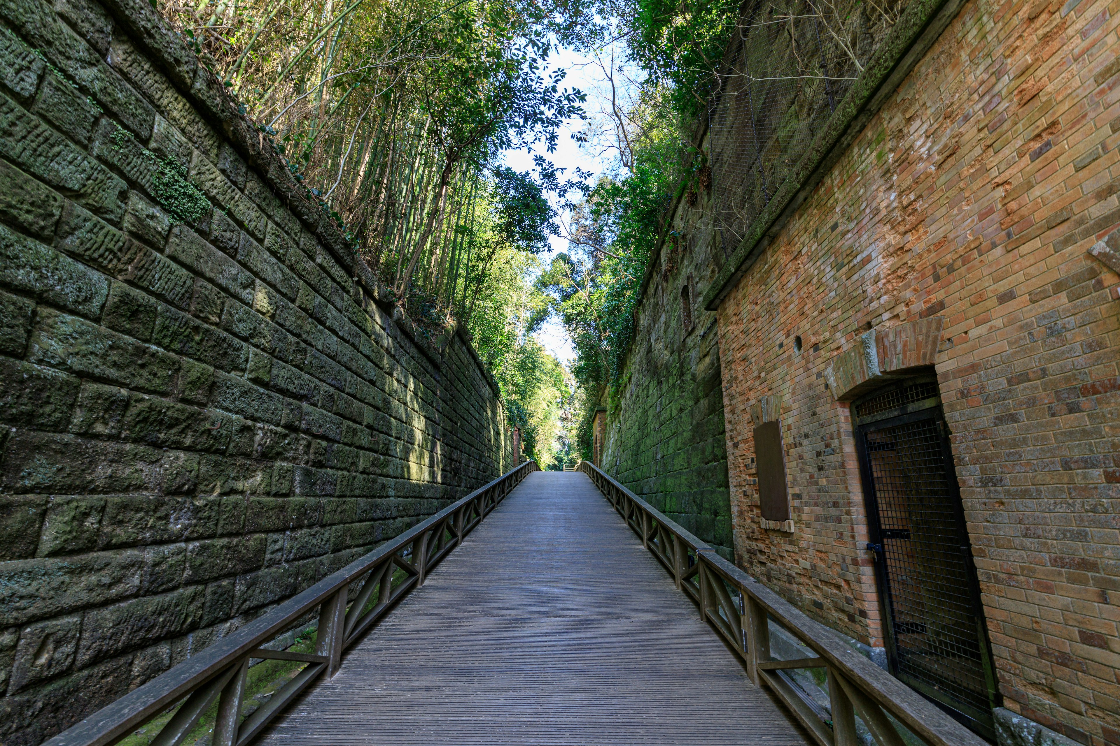 Sentiero panoramico fiancheggiato da muri di pietra e strutture in mattoni circondato da vegetazione lussureggiante