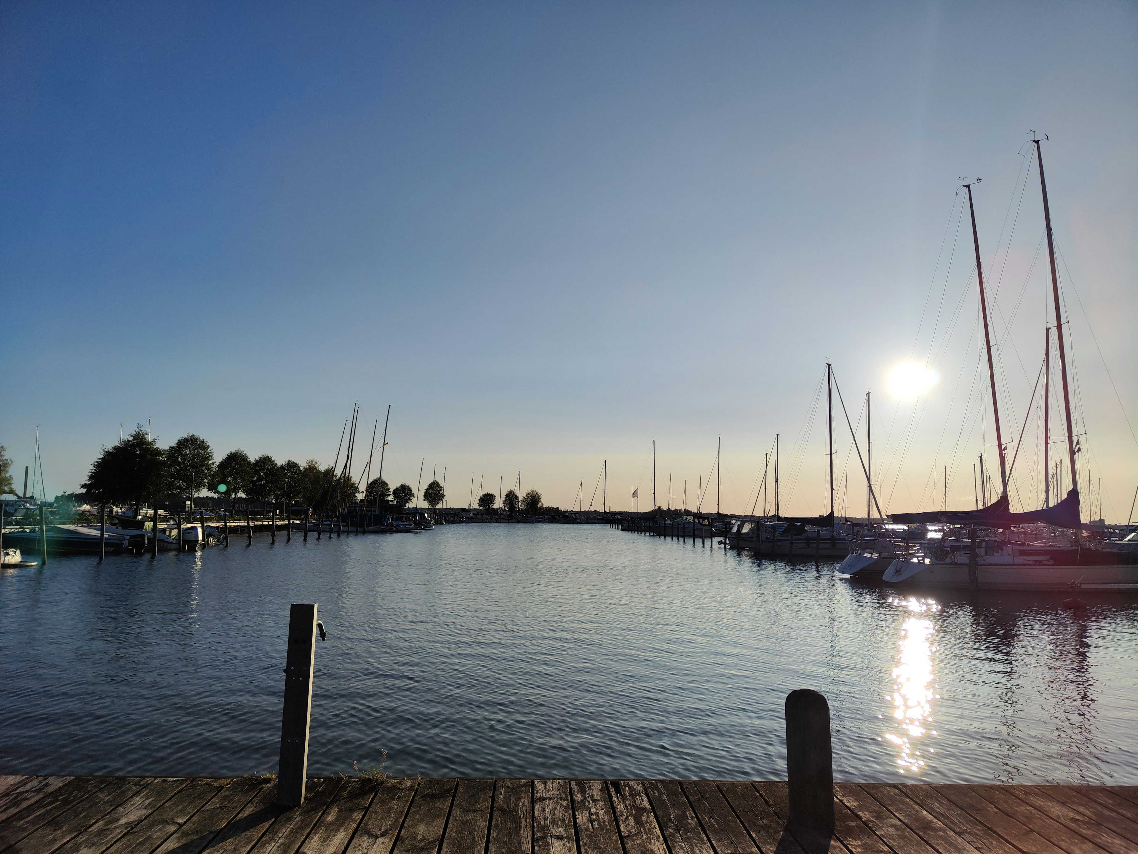 Calm waterfront scene with sunset reflection and moored sailboats