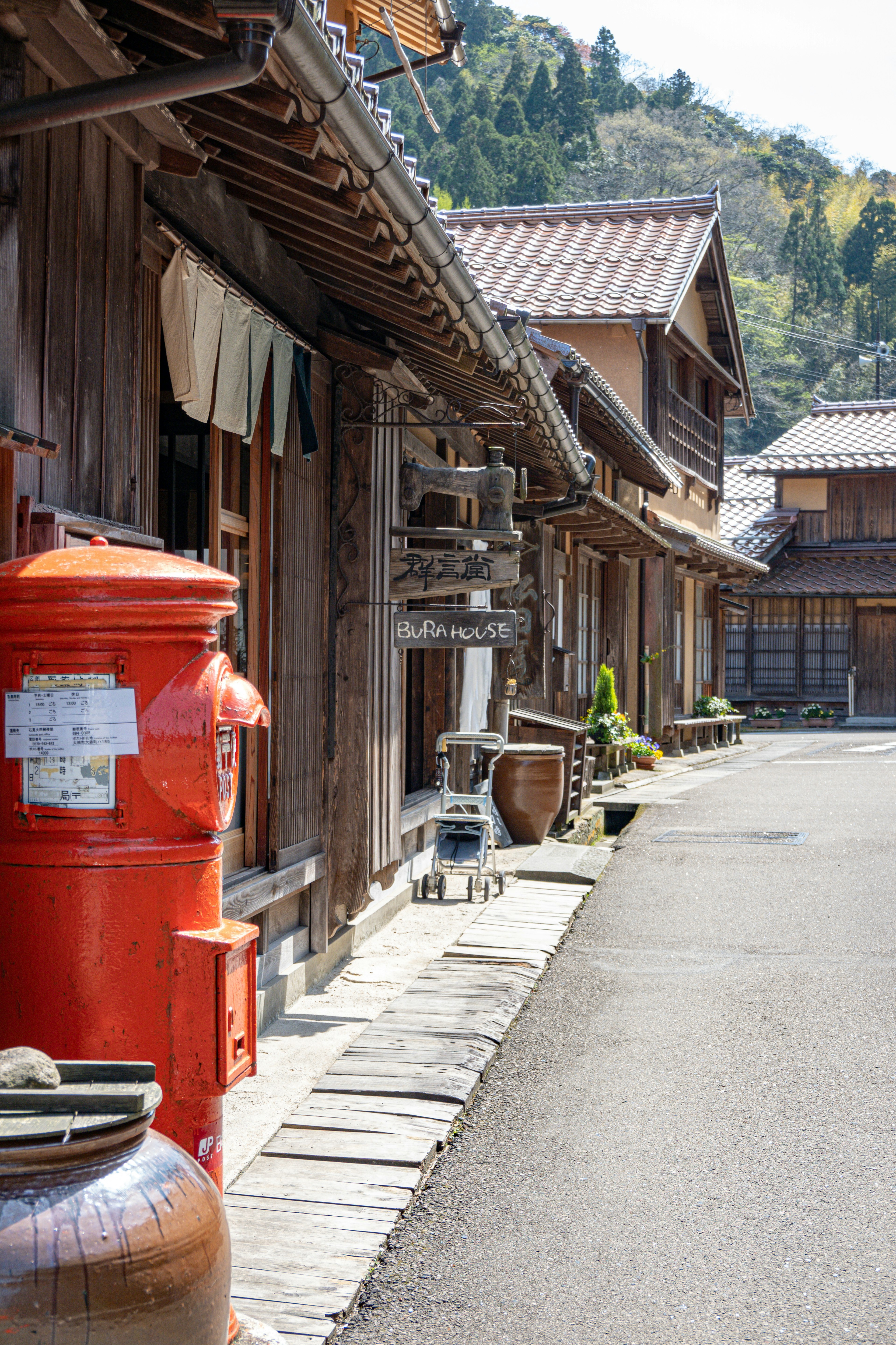 古い木造の建物が並ぶ通りに赤い郵便ポストがある風景