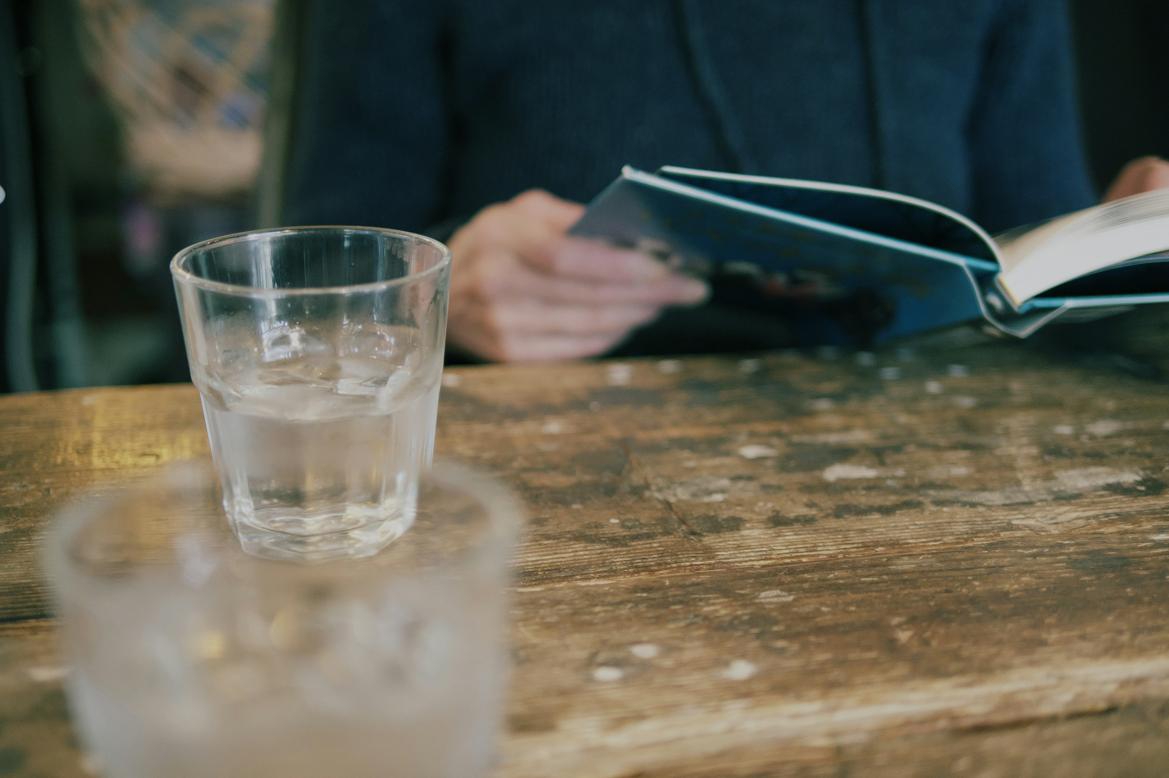 A cafe scene with a glass of water and a person's hand reading a book