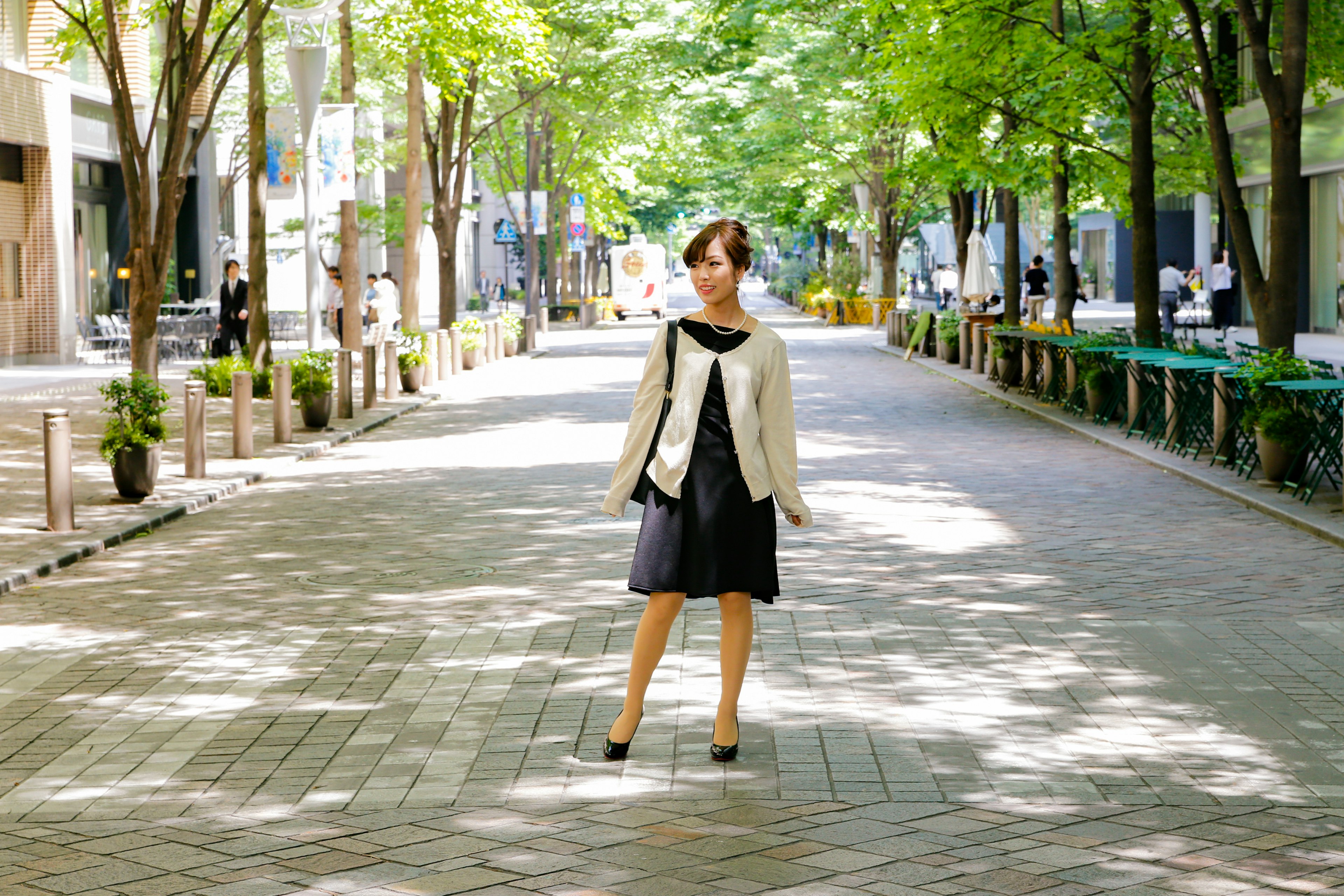 A woman standing in a tree-lined street wearing a stylish outfit