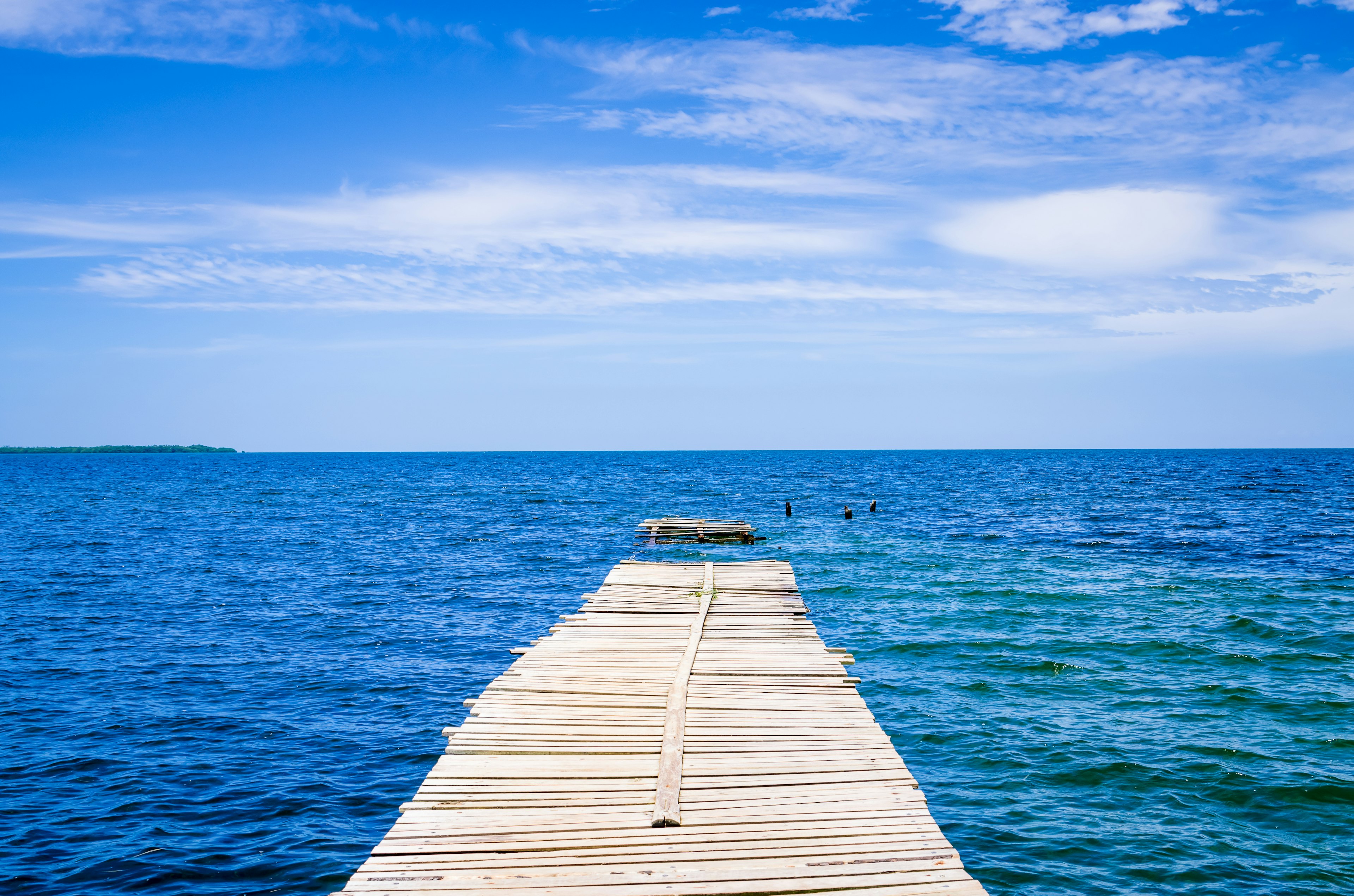 Holzsteg, der ins blaue Meer unter einem hellen Himmel führt