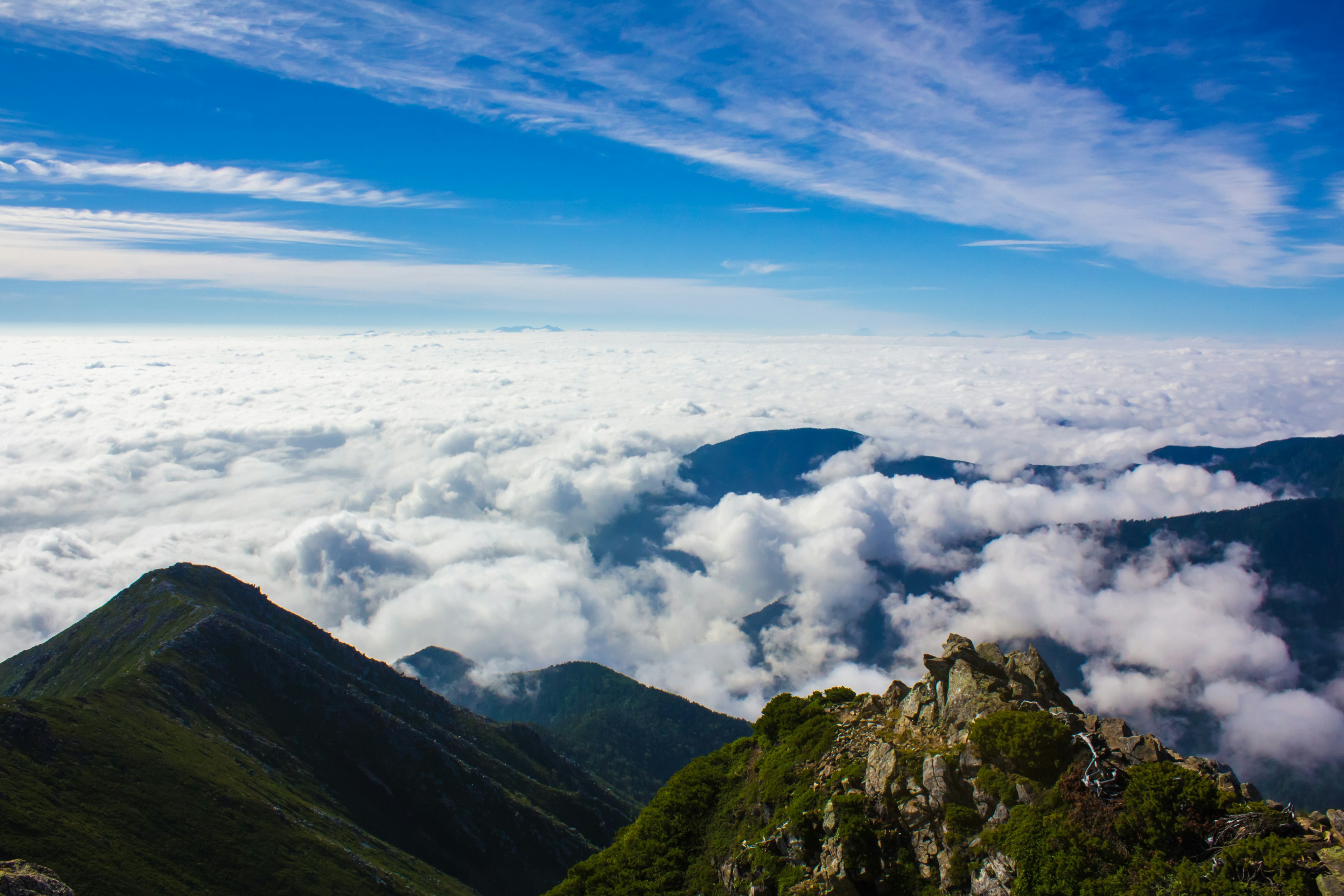 Panoramablick von einem Berggipfel über ein Wolkenmeer und einen blauen Himmel