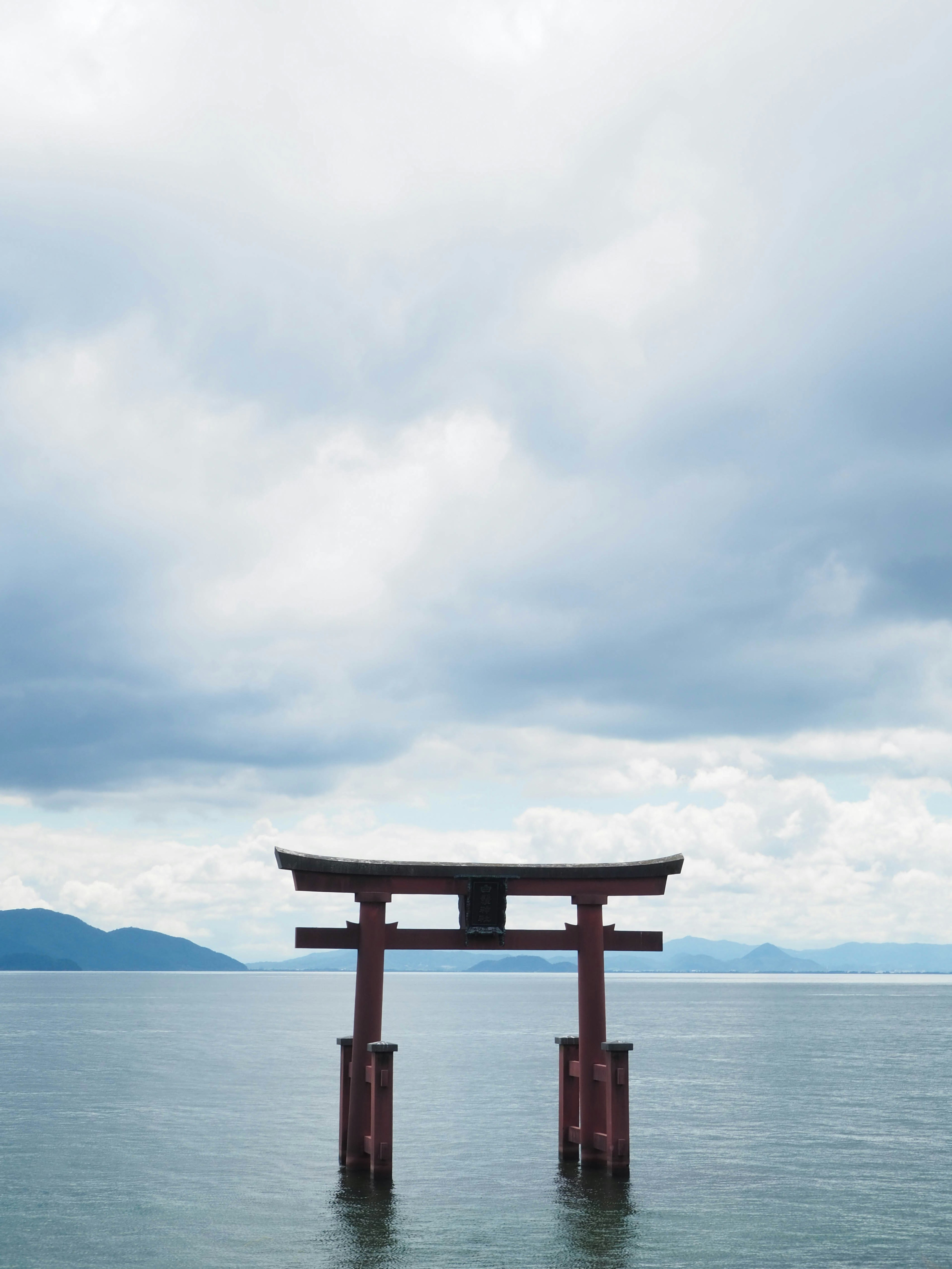 Torii yang berdiri di atas air dengan langit mendung