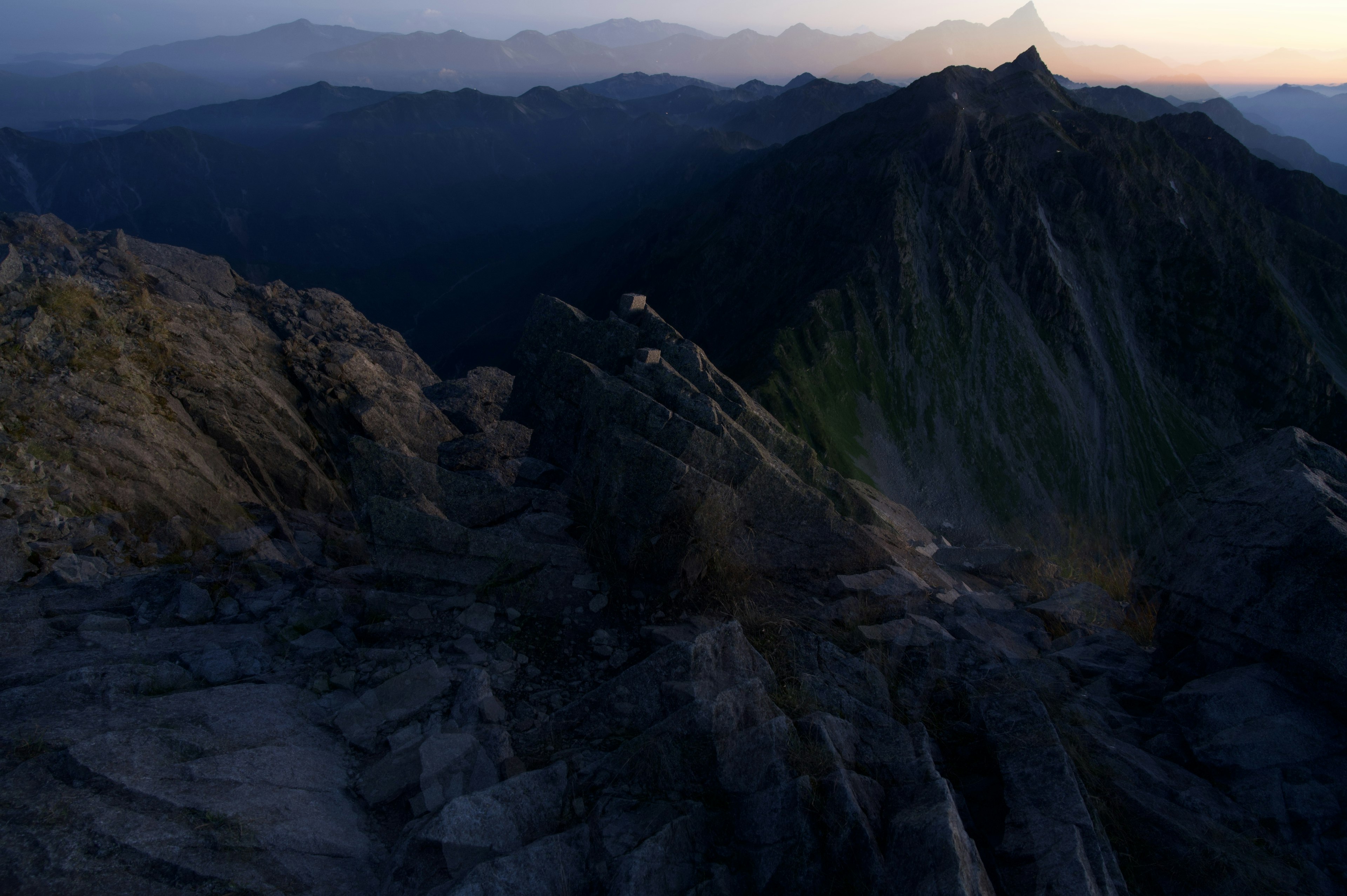 Paisaje montañoso dramático al atardecer con primer plano rocoso y picos distantes