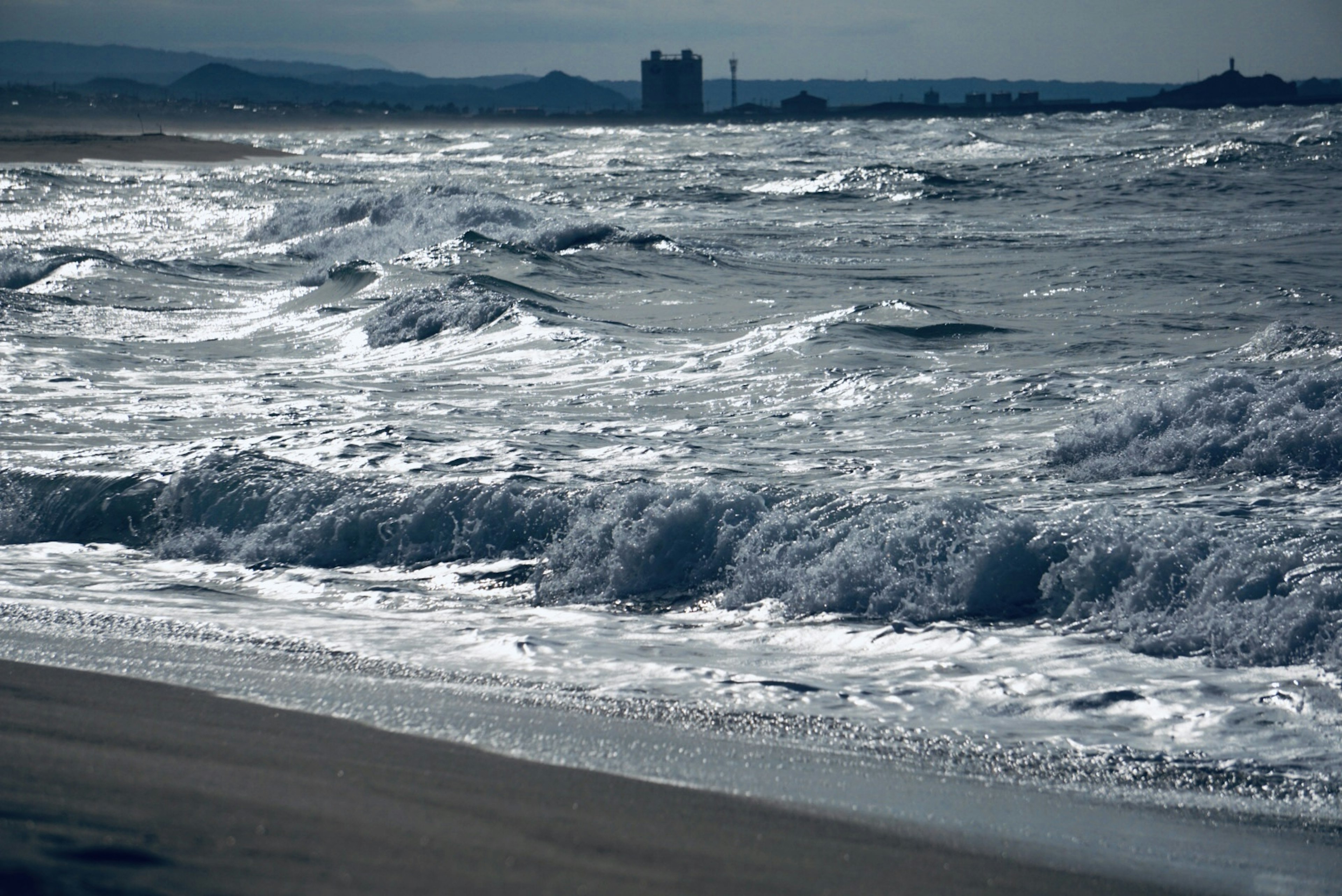 Rough sea waves along a coastline with distant buildings in the background