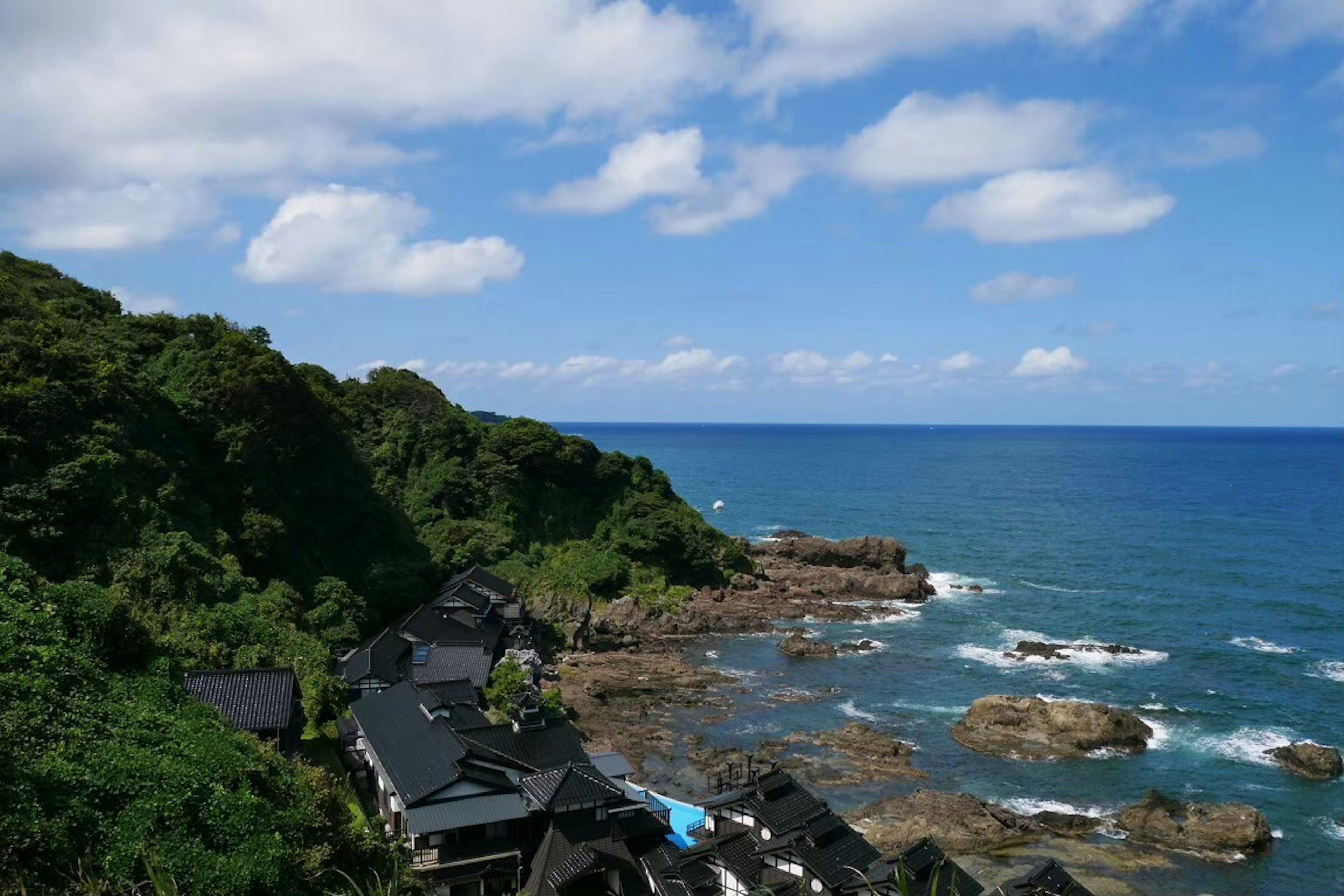 Scenic view of ocean and rocky shoreline lush green hills and blue sky