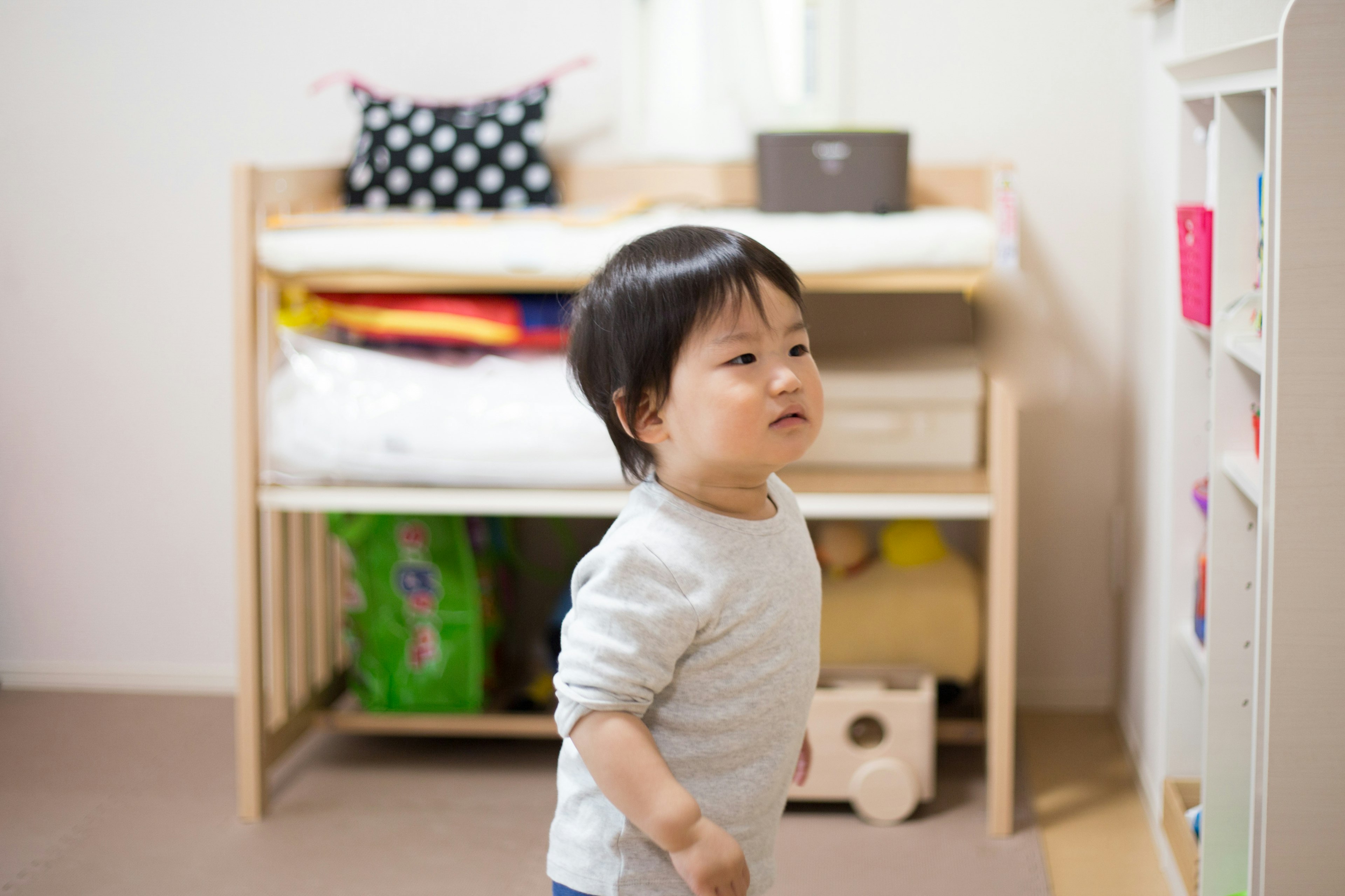 子供が部屋の棚の前に立っている様子でカラフルな本やおもちゃが見える