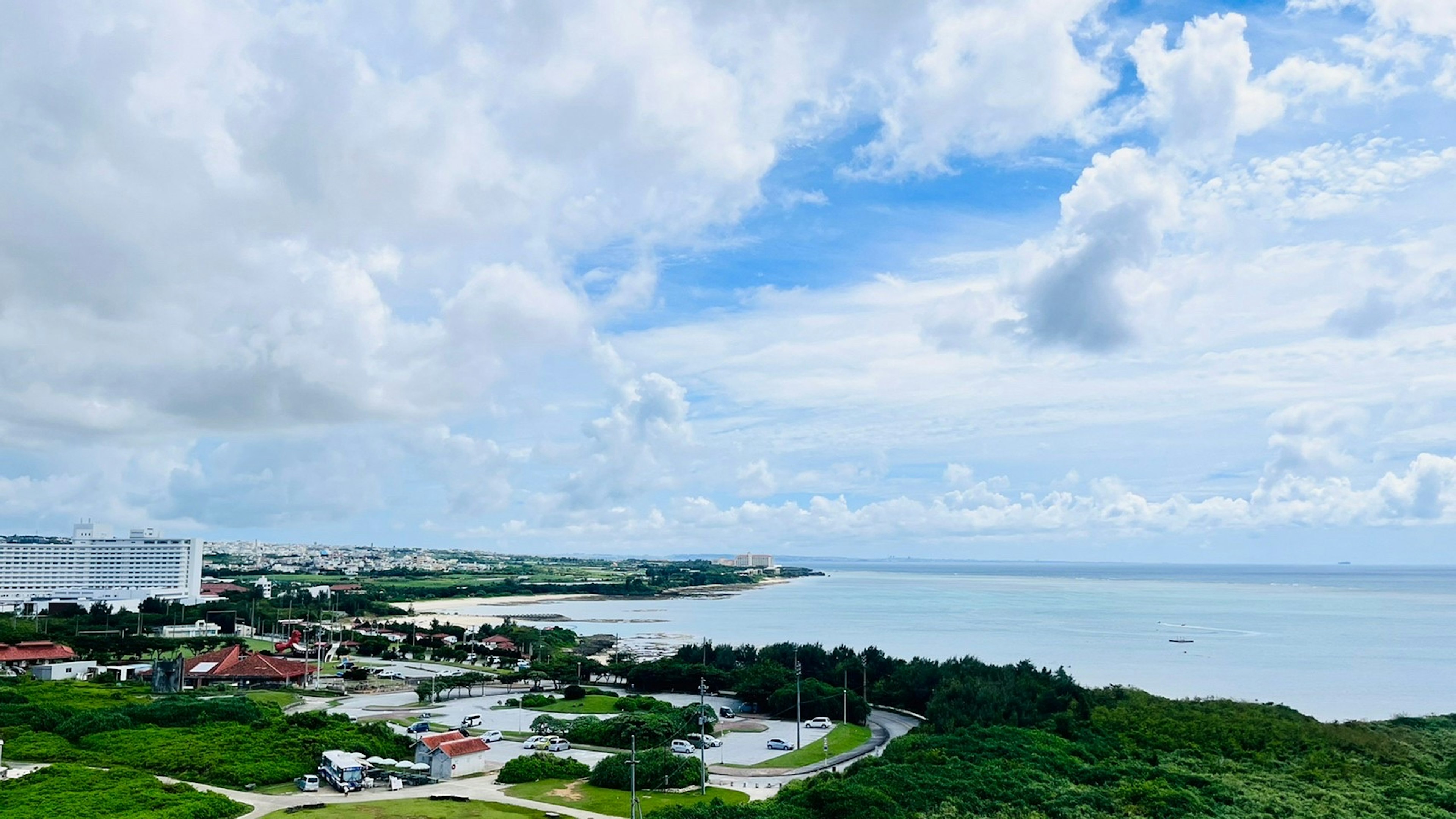 Scenic view of blue ocean and white clouds with green hills and buildings