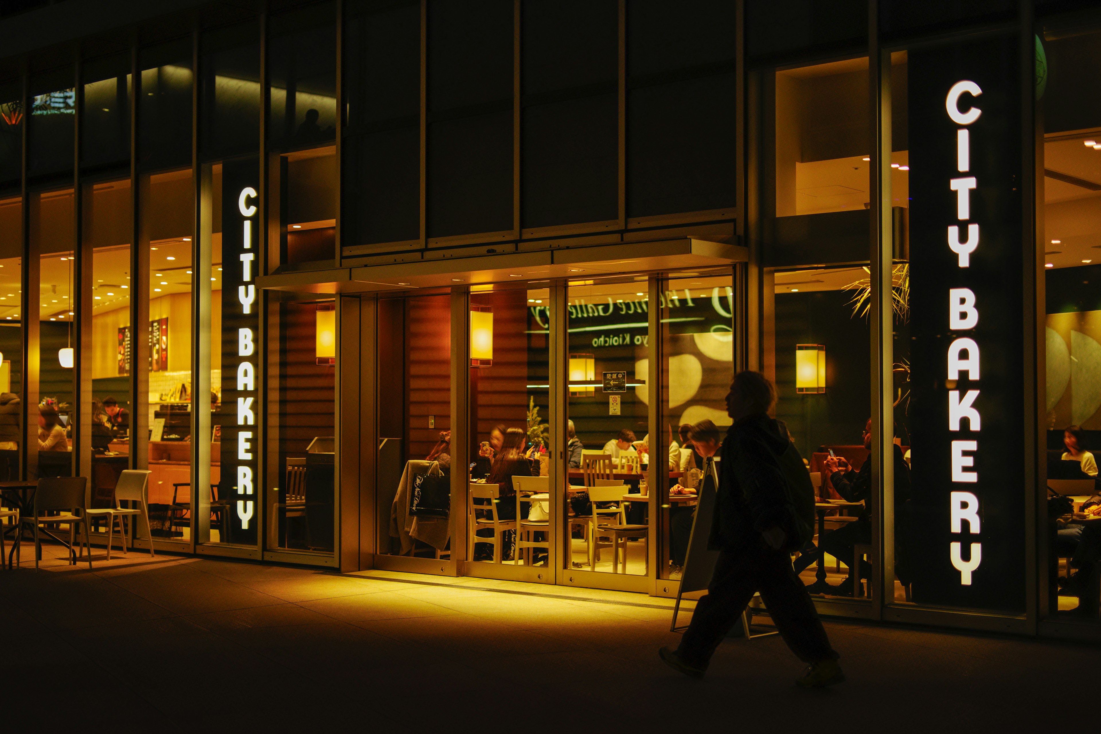 Exterior de City Bakery de noche con comensales dentro