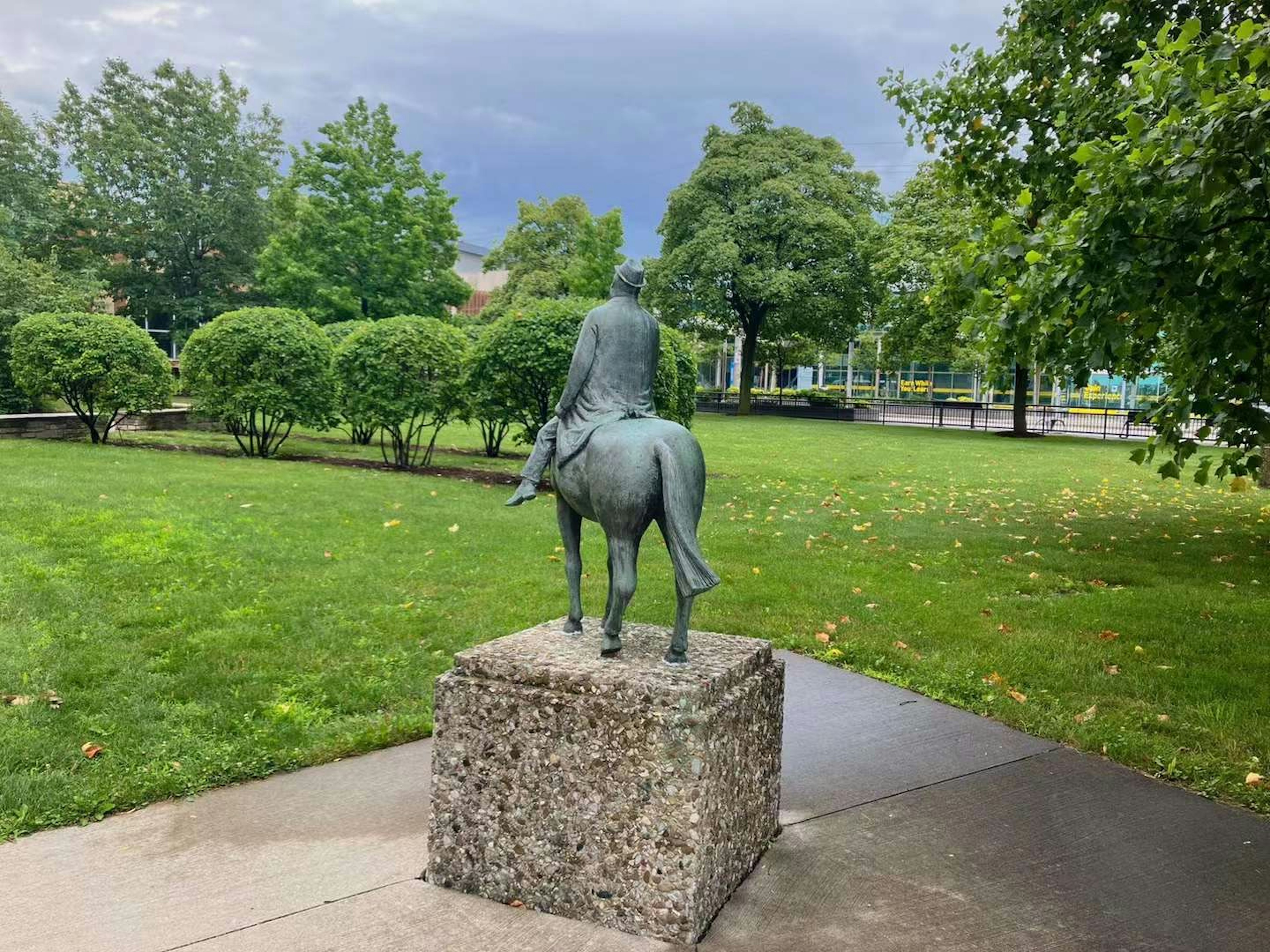 Bronze statue of a person riding a cow in a green park