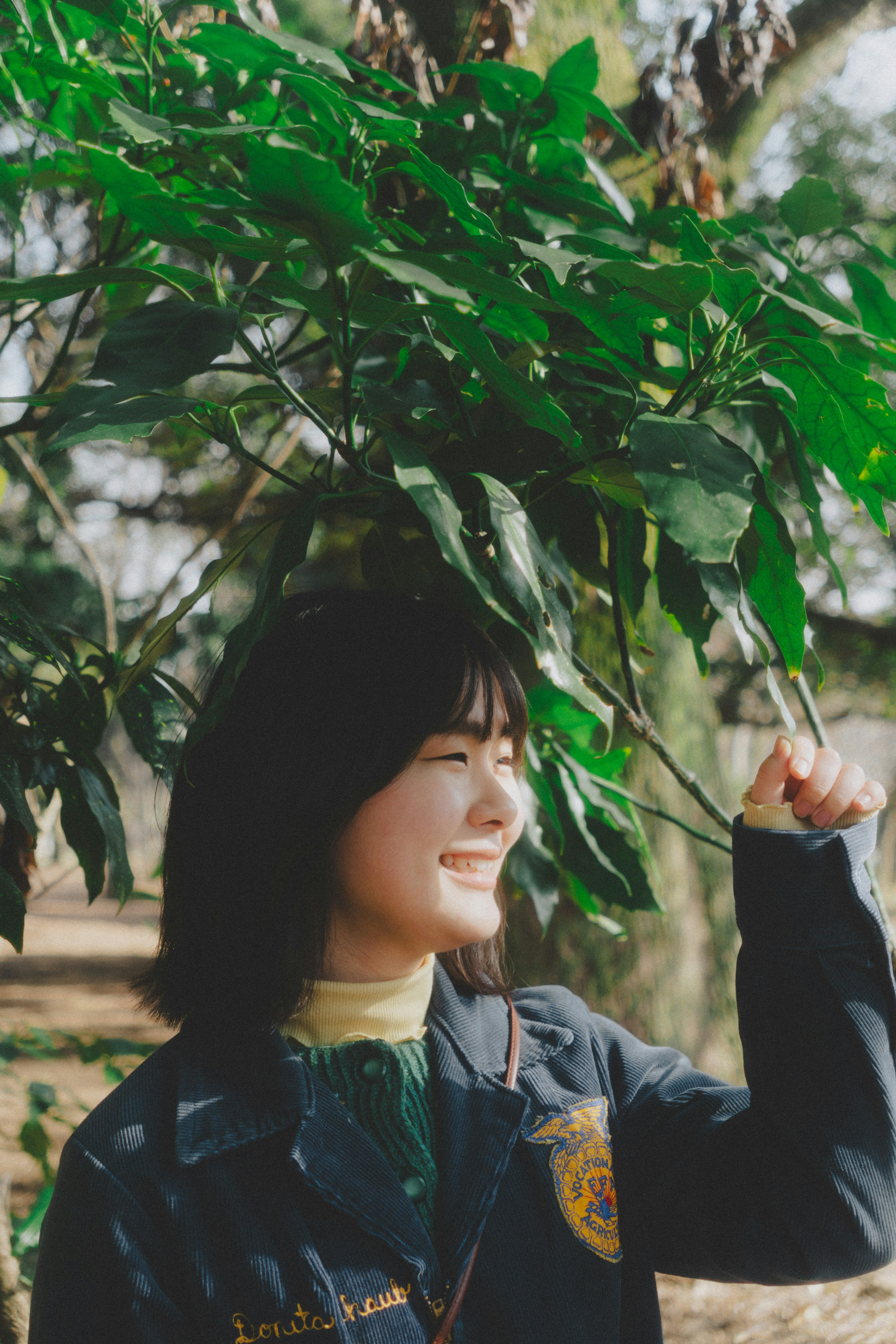 Wanita tersenyum di bawah daun hijau