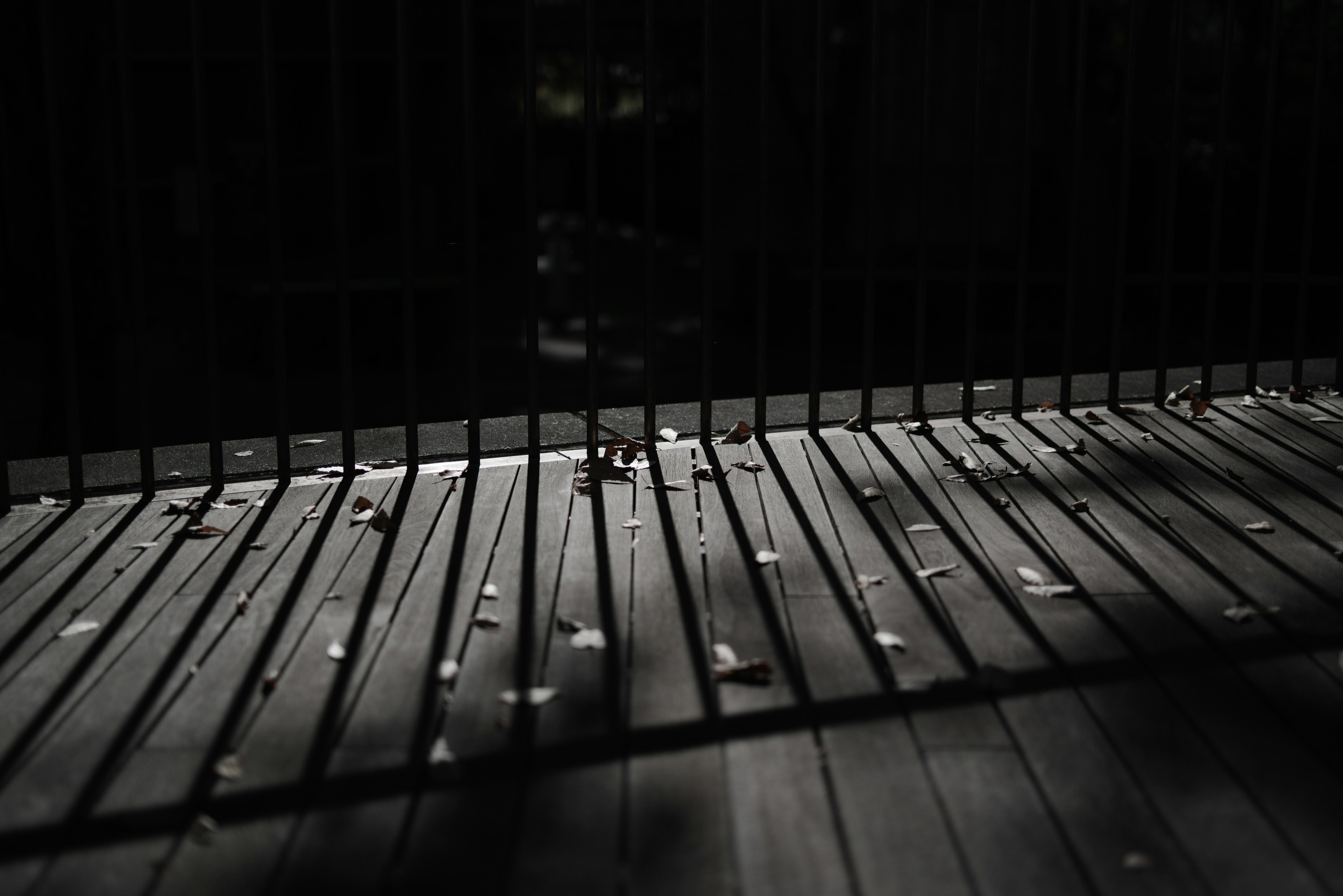 Escena con una terraza de madera y sombras de una cerca en un entorno oscuro