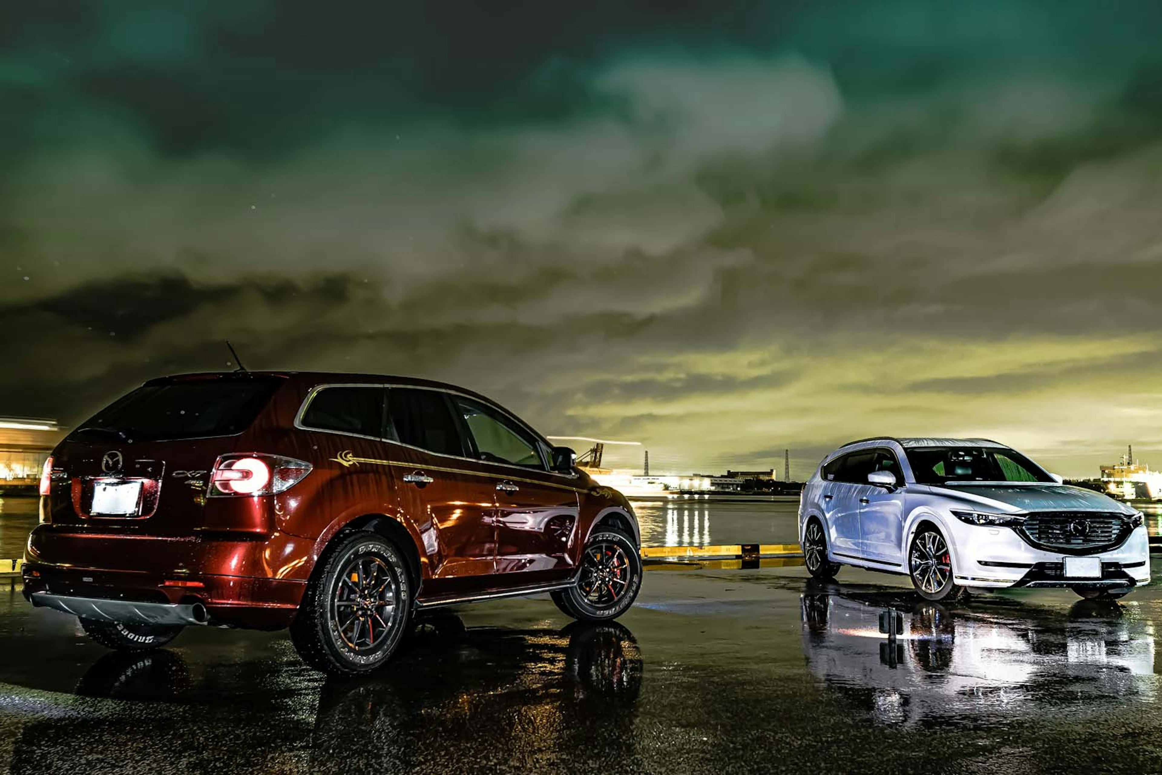 Red SUV and white sedan parked on a rain-soaked surface in a nighttime setting