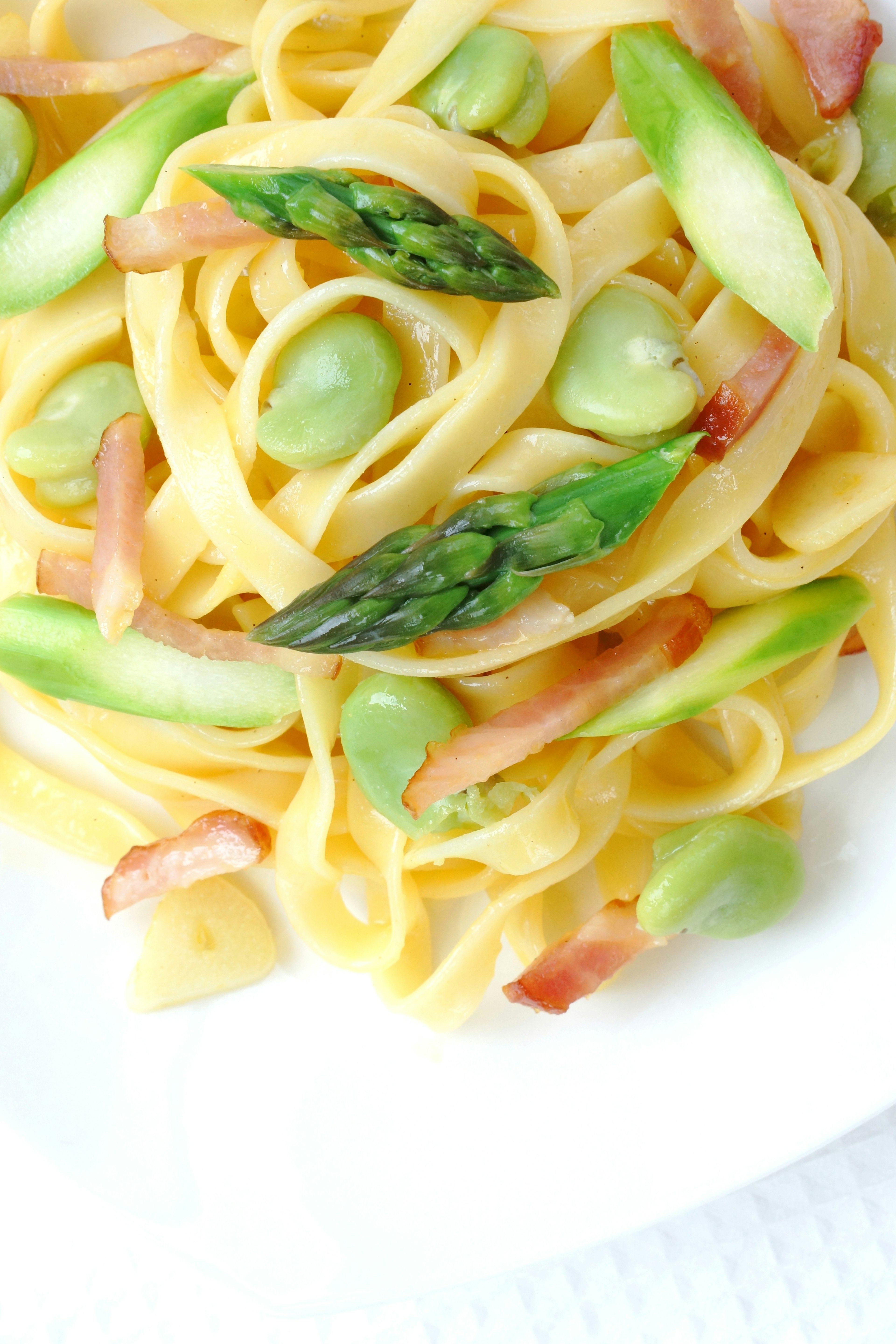 Piatto di pasta guarnito con asparagi e pancetta in una salsa cremosa