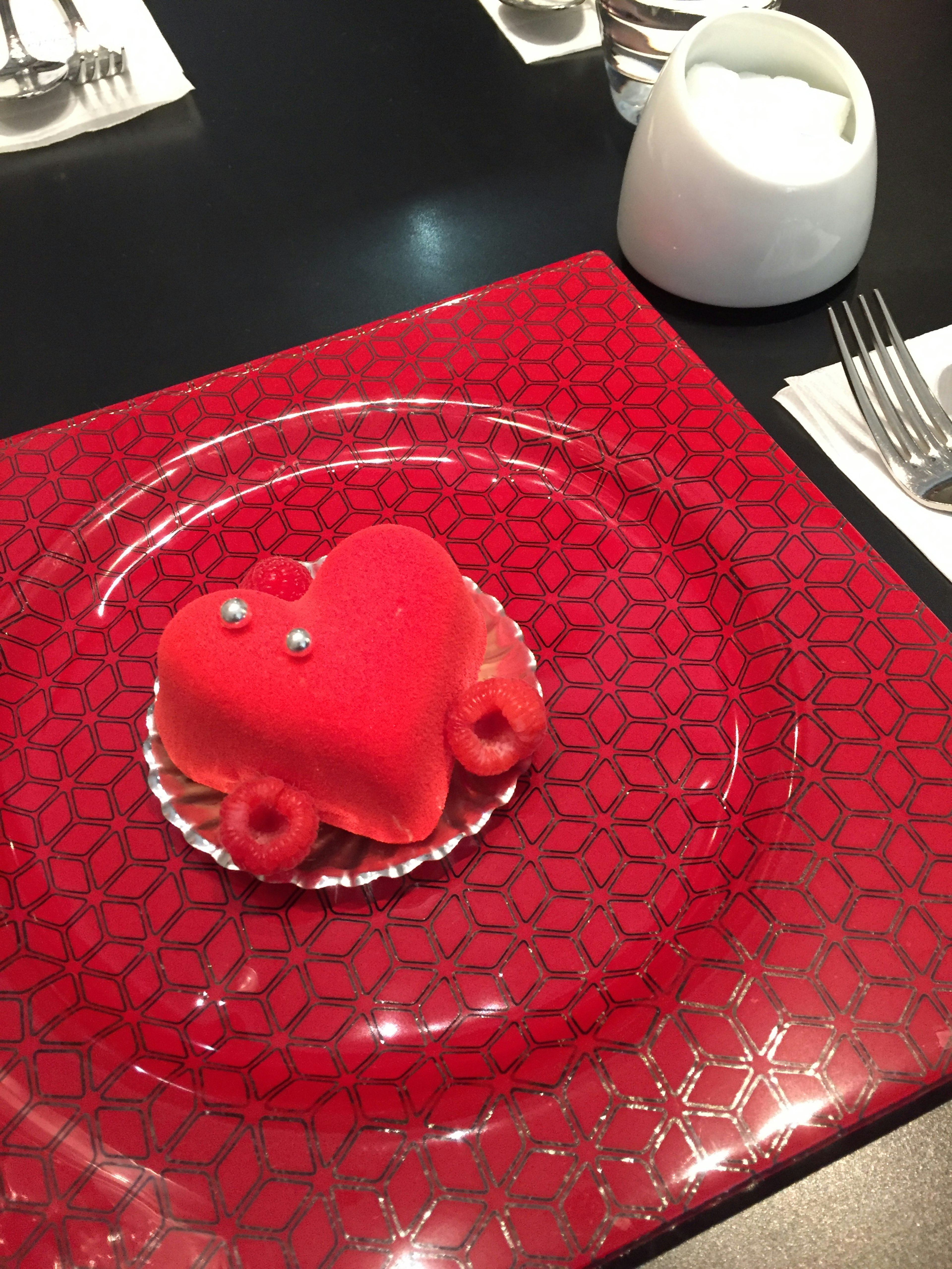 Red heart-shaped dessert on a decorative plate set on a table