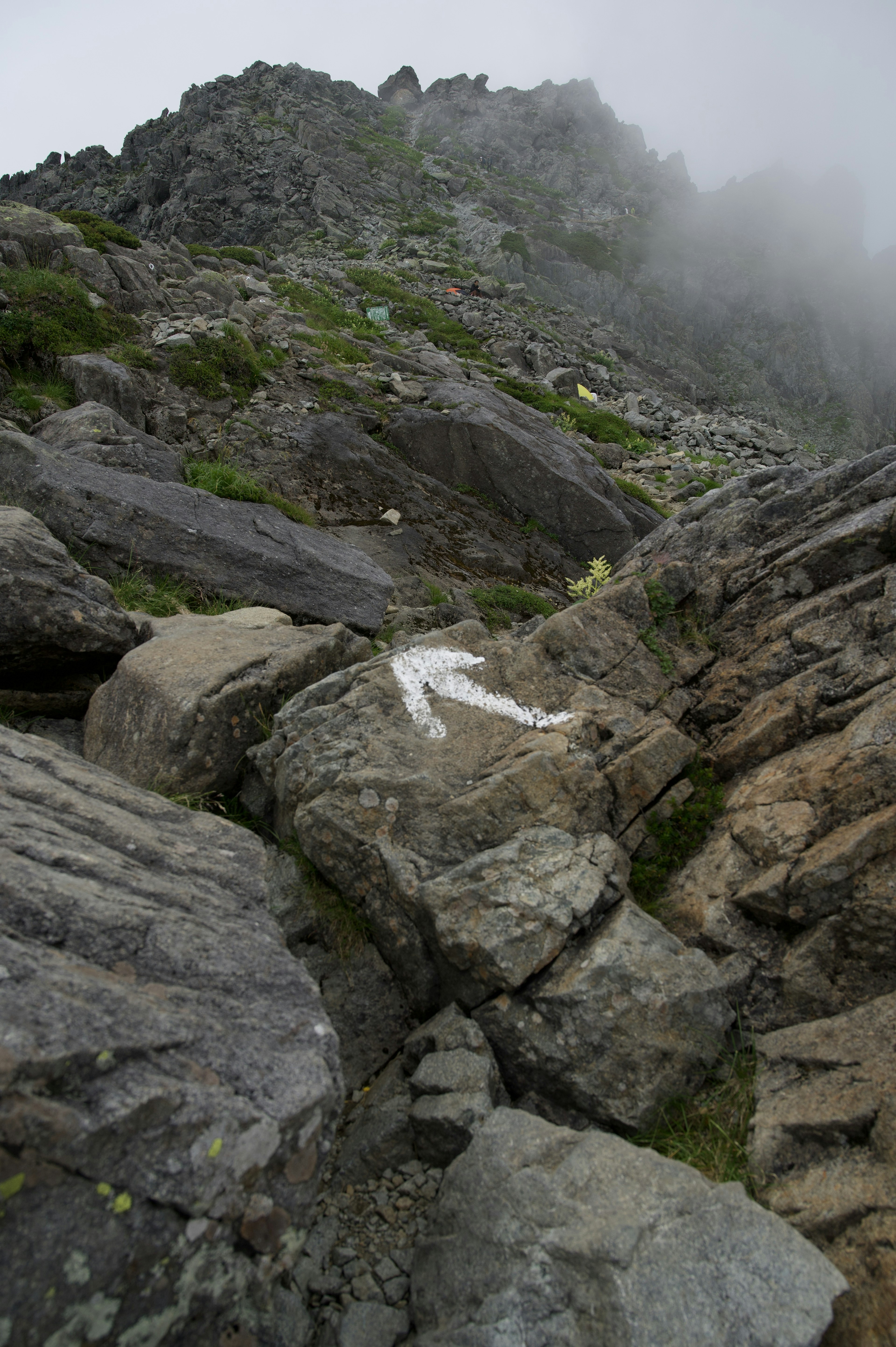 Segno di freccia bianca su una montagna rocciosa nella nebbia