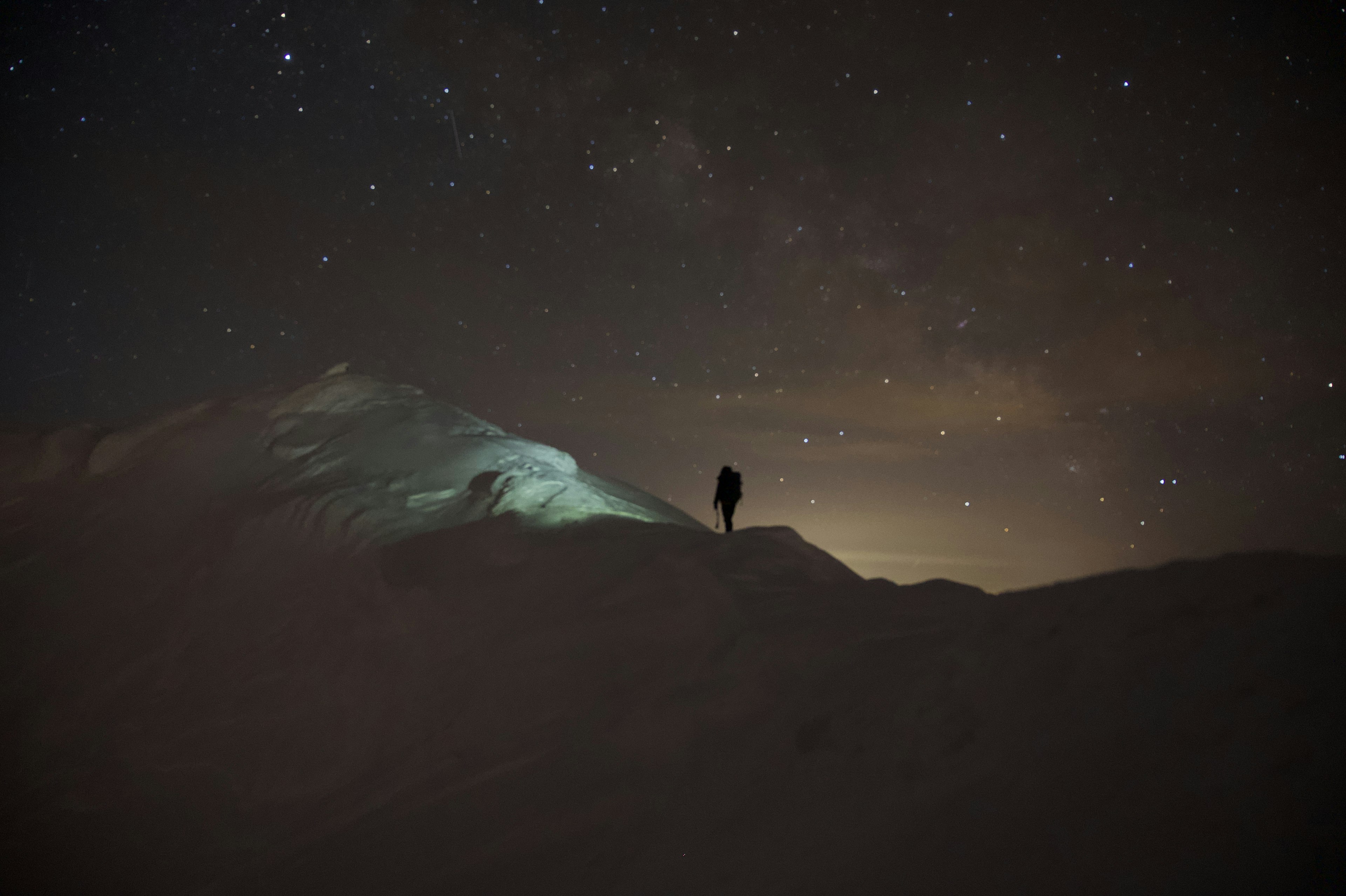 暗い山の頂上に立つ人のシルエットと星が輝く夜空