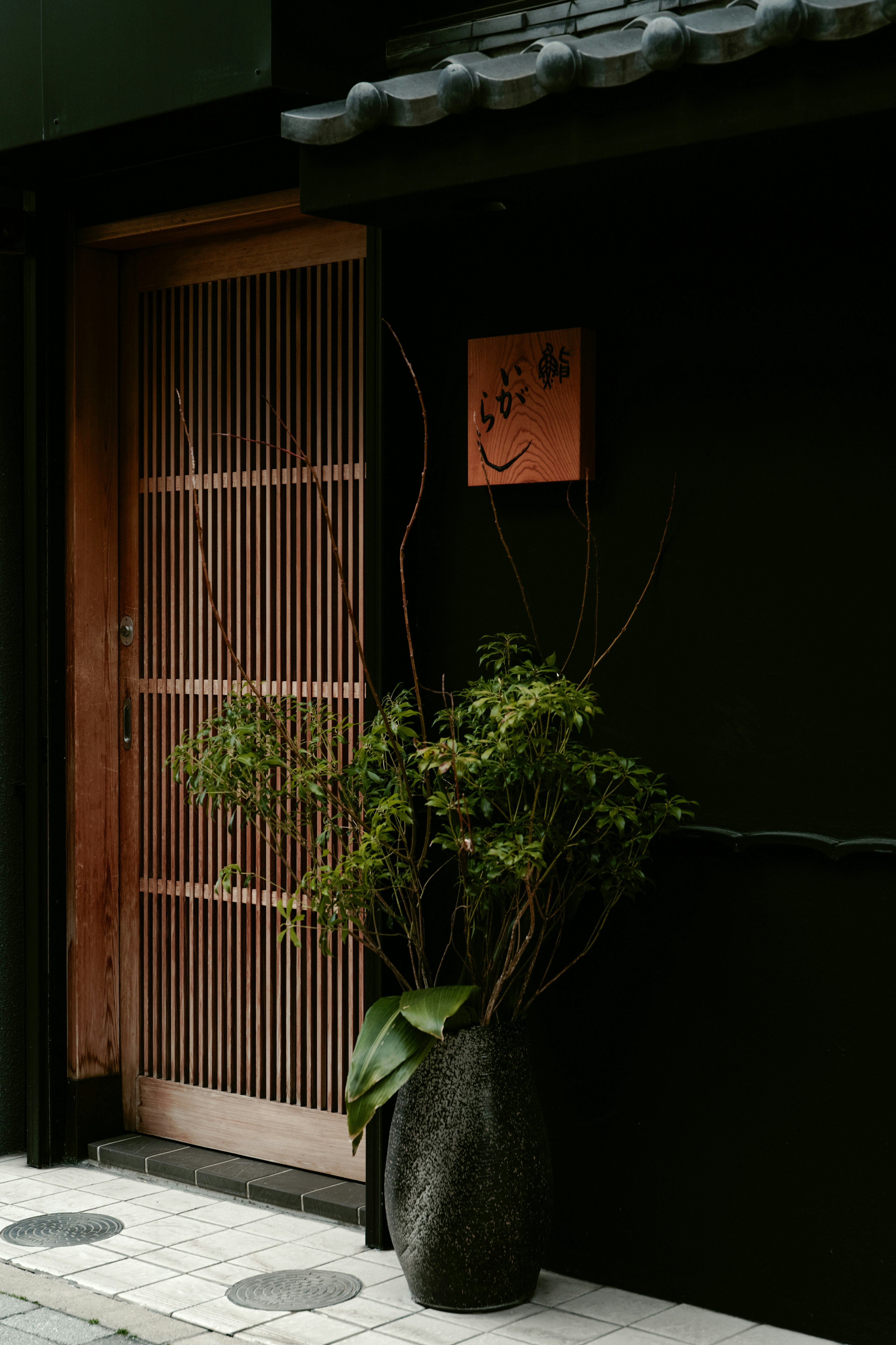 Puerta corrediza de bambú frente a una pared negra con una planta en maceta