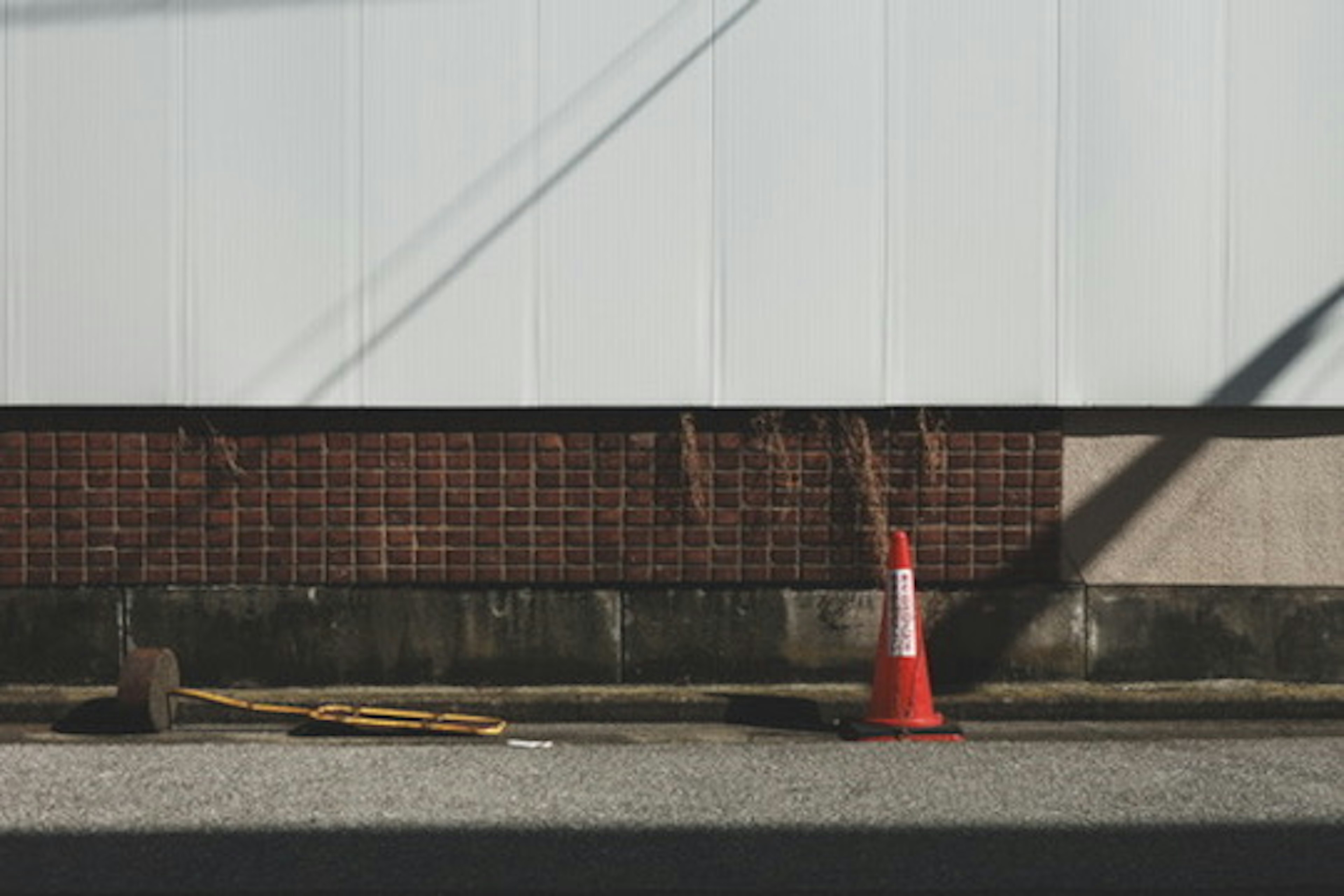 Cono de tráfico rojo junto a herramientas en la calle junto a una pared blanca