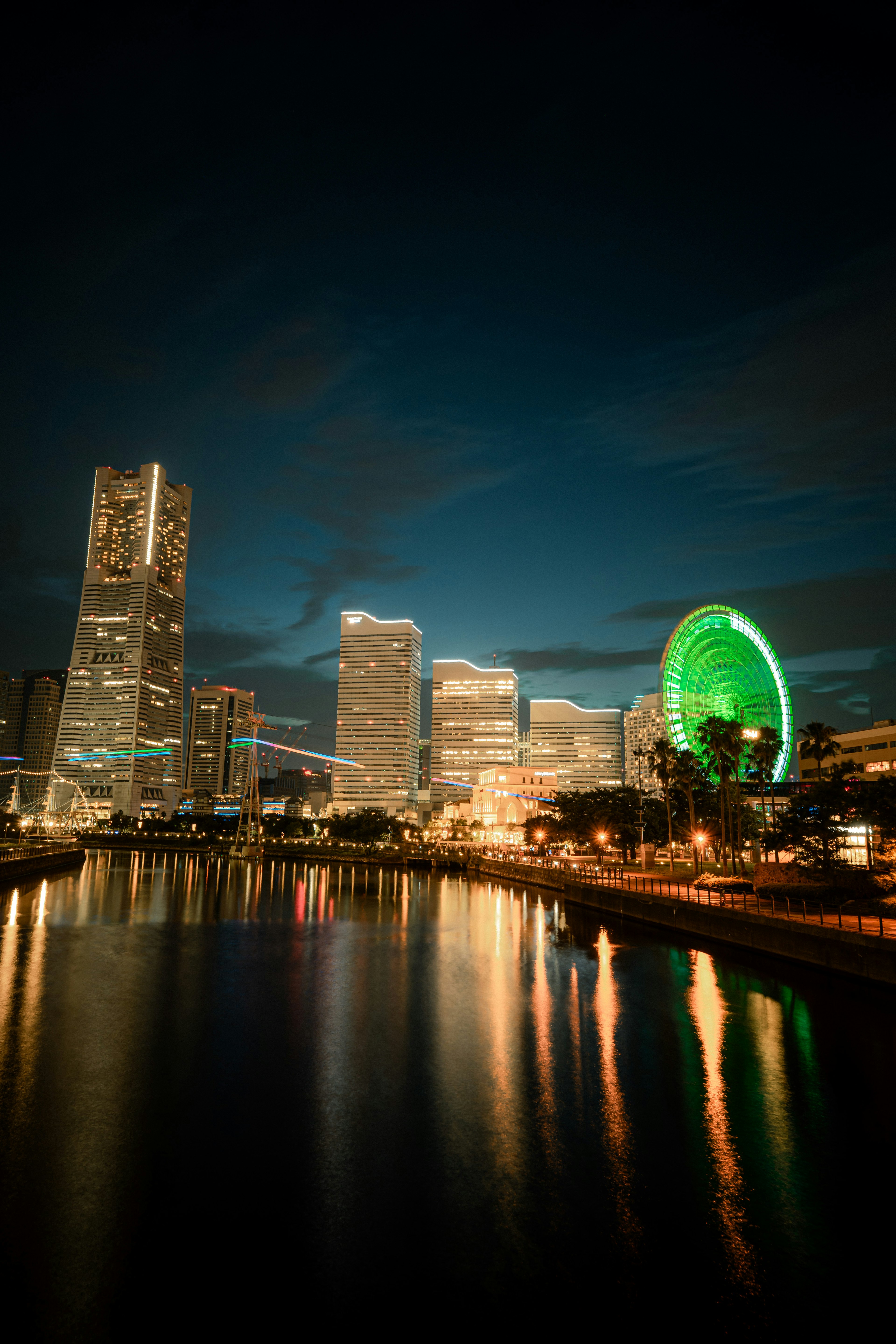 夜间城市景观，灯光闪烁的摩天大楼和绿色摩天轮在水中倒影