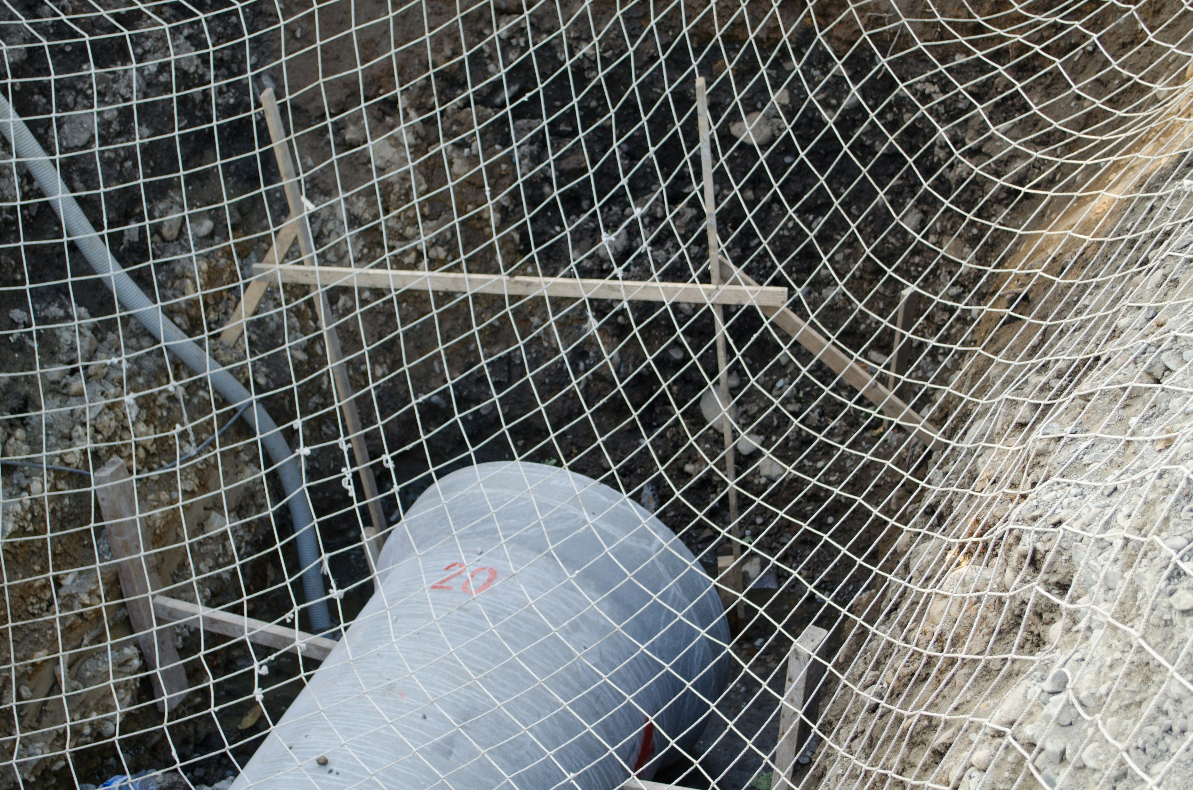 Partie d'un chantier de construction avec un filet visible ainsi que des tuyaux métalliques et du béton