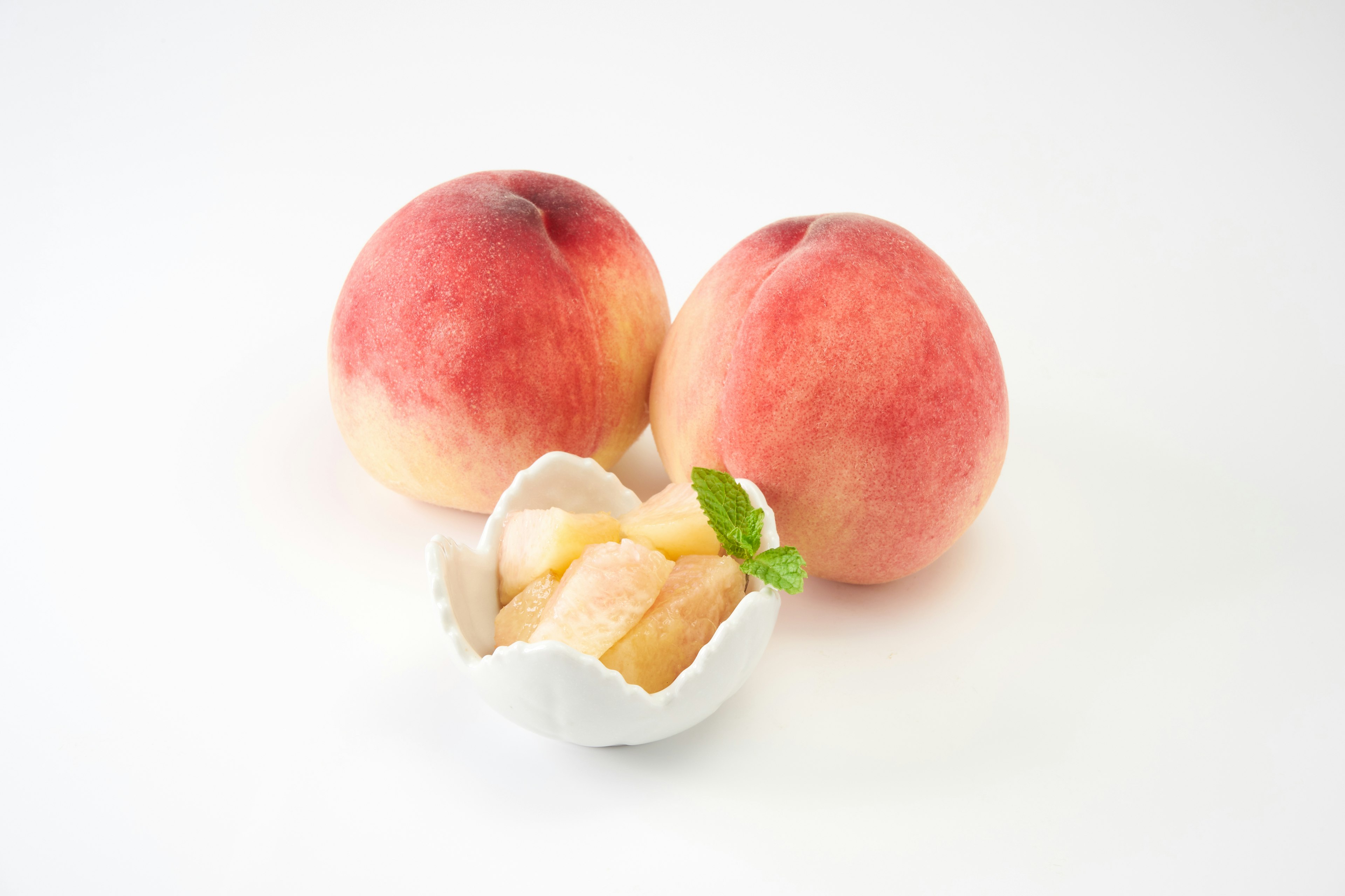 Two peaches and sliced peach in a white dish